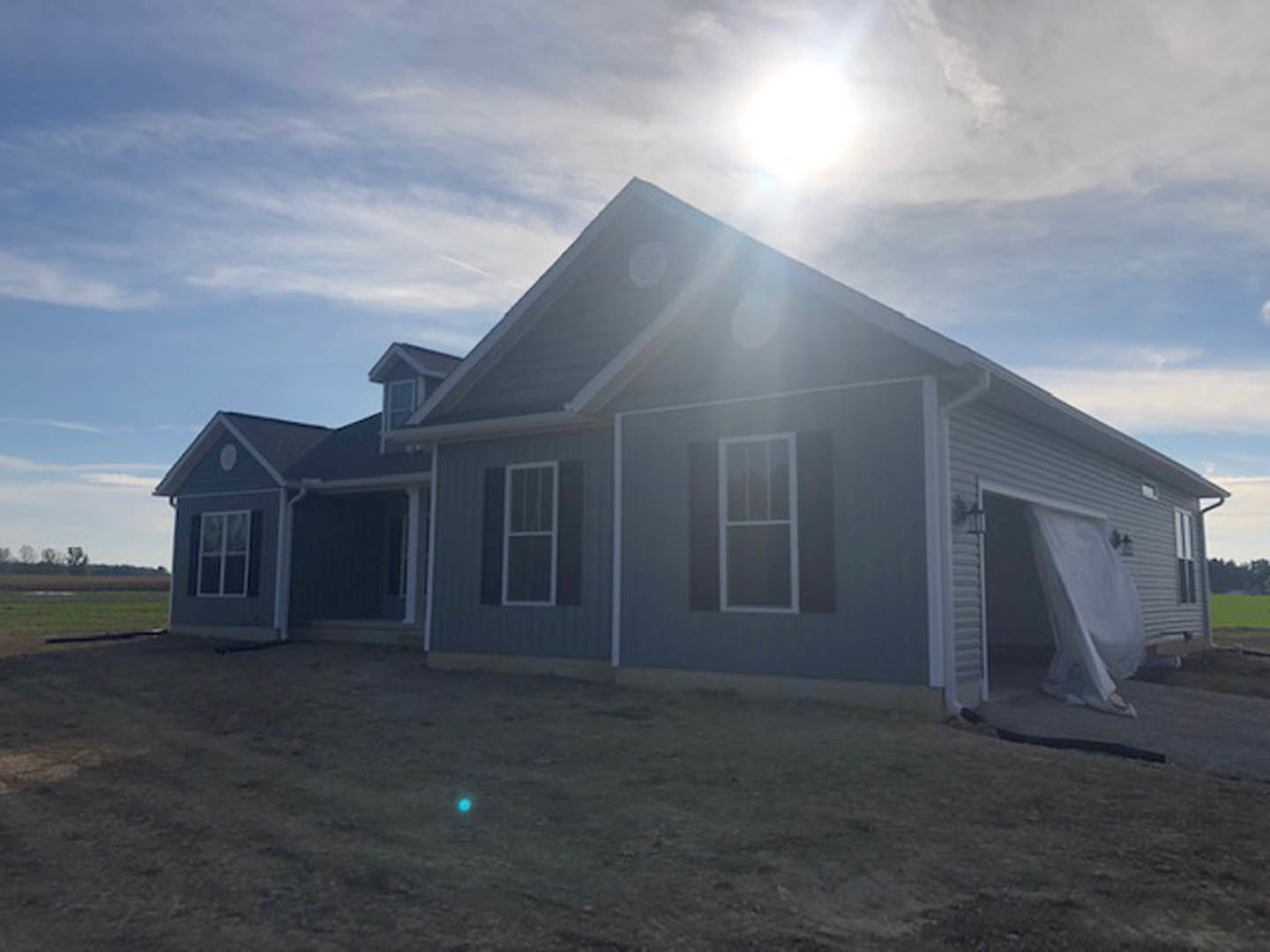 Two-story house with blue roof, white siding, white door with glass panes, white-framed windows, green grass lawn, blue sky with scattered clouds