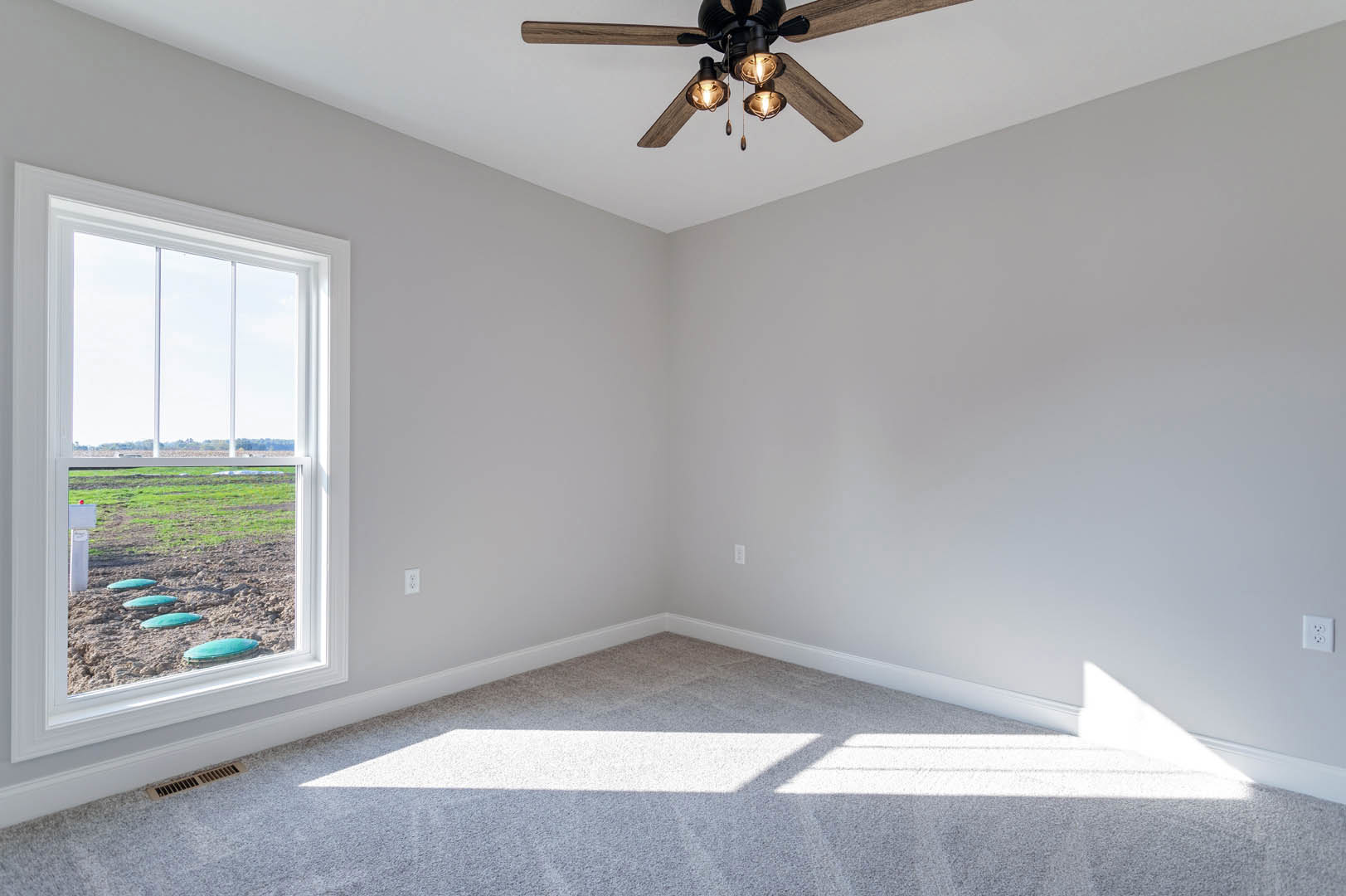 Carpeted room corner with white walls, ceiling fan with light fixture, large window overlooking grassy field, crown molding along ceiling.