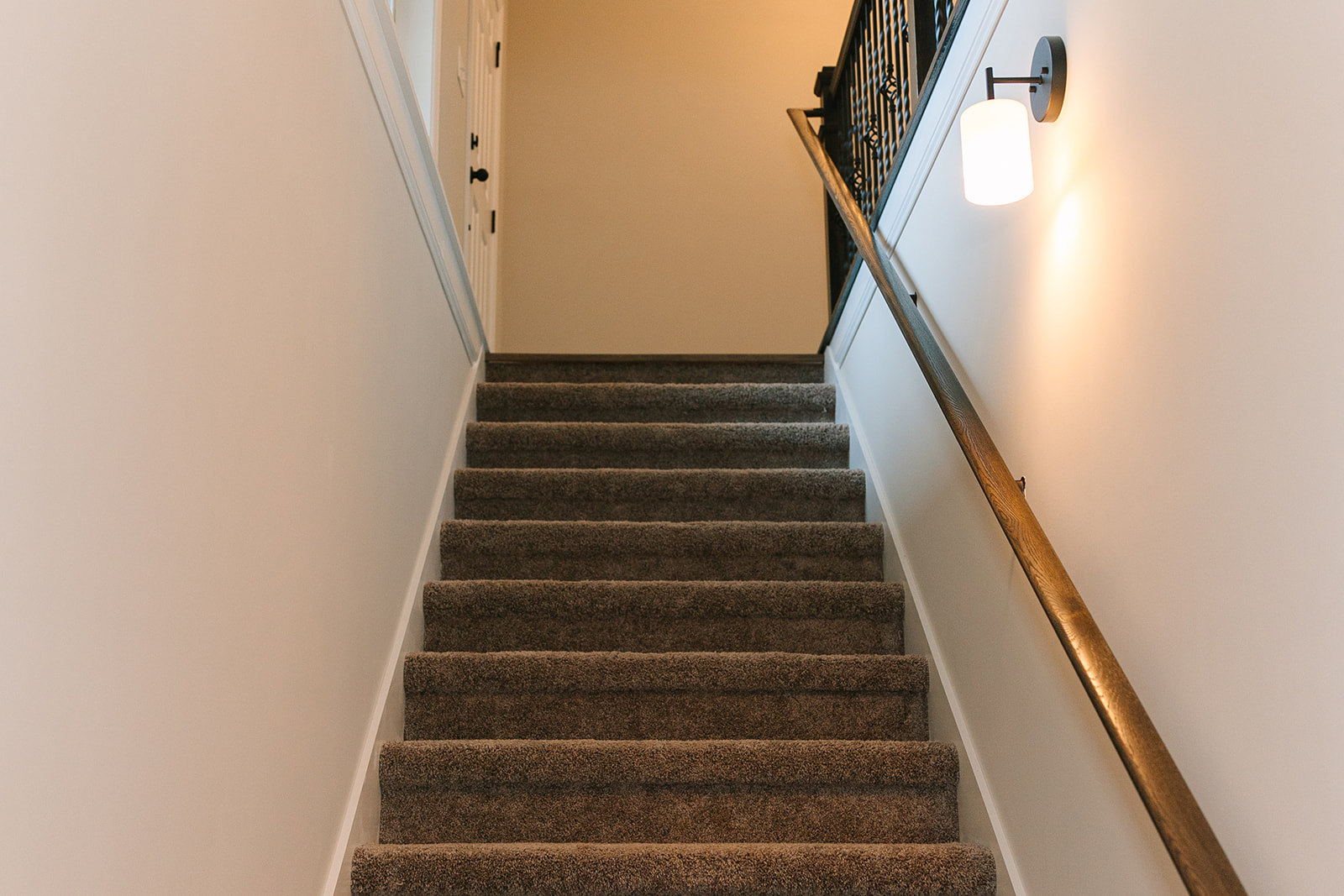 Carpeted staircase with white handrail and wall-mounted sconce light, neutral painted walls