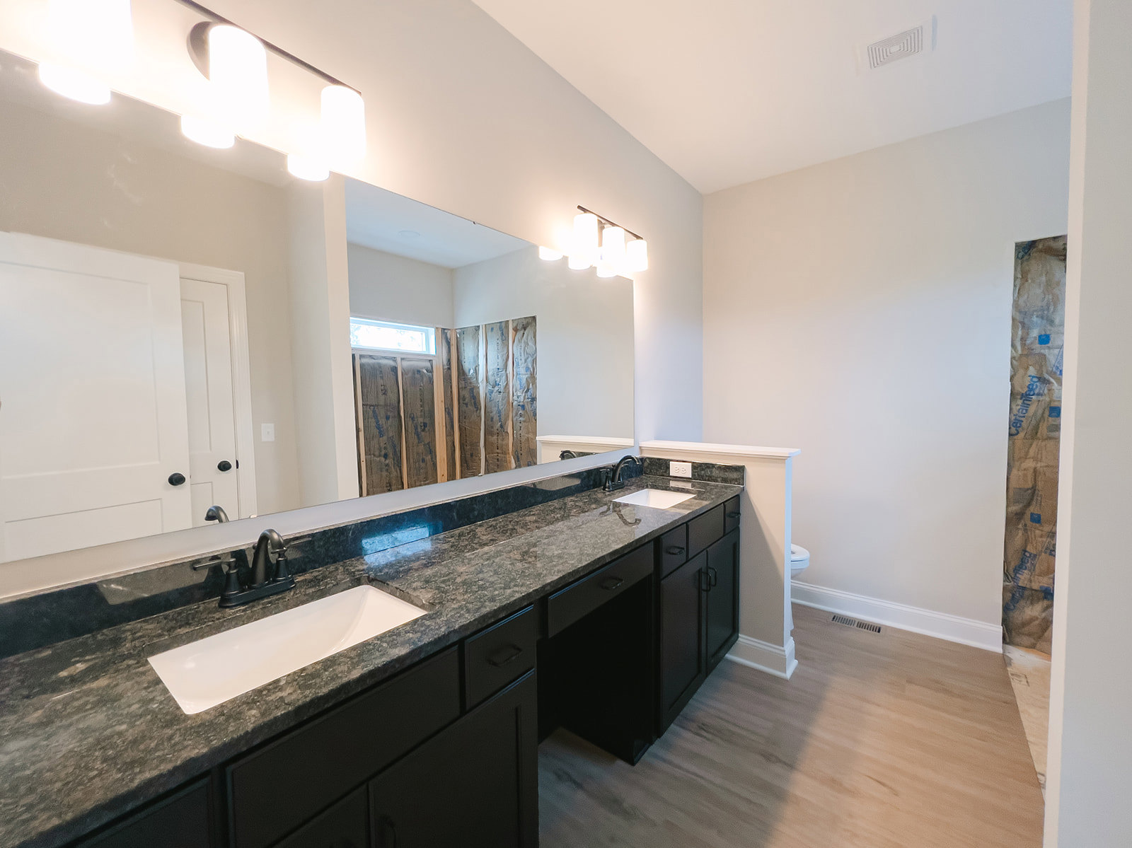 Bathroom with expansive mirror above black granite countertop, white undermount sink, matte black faucet, light tile walls, and modern cabinetry.