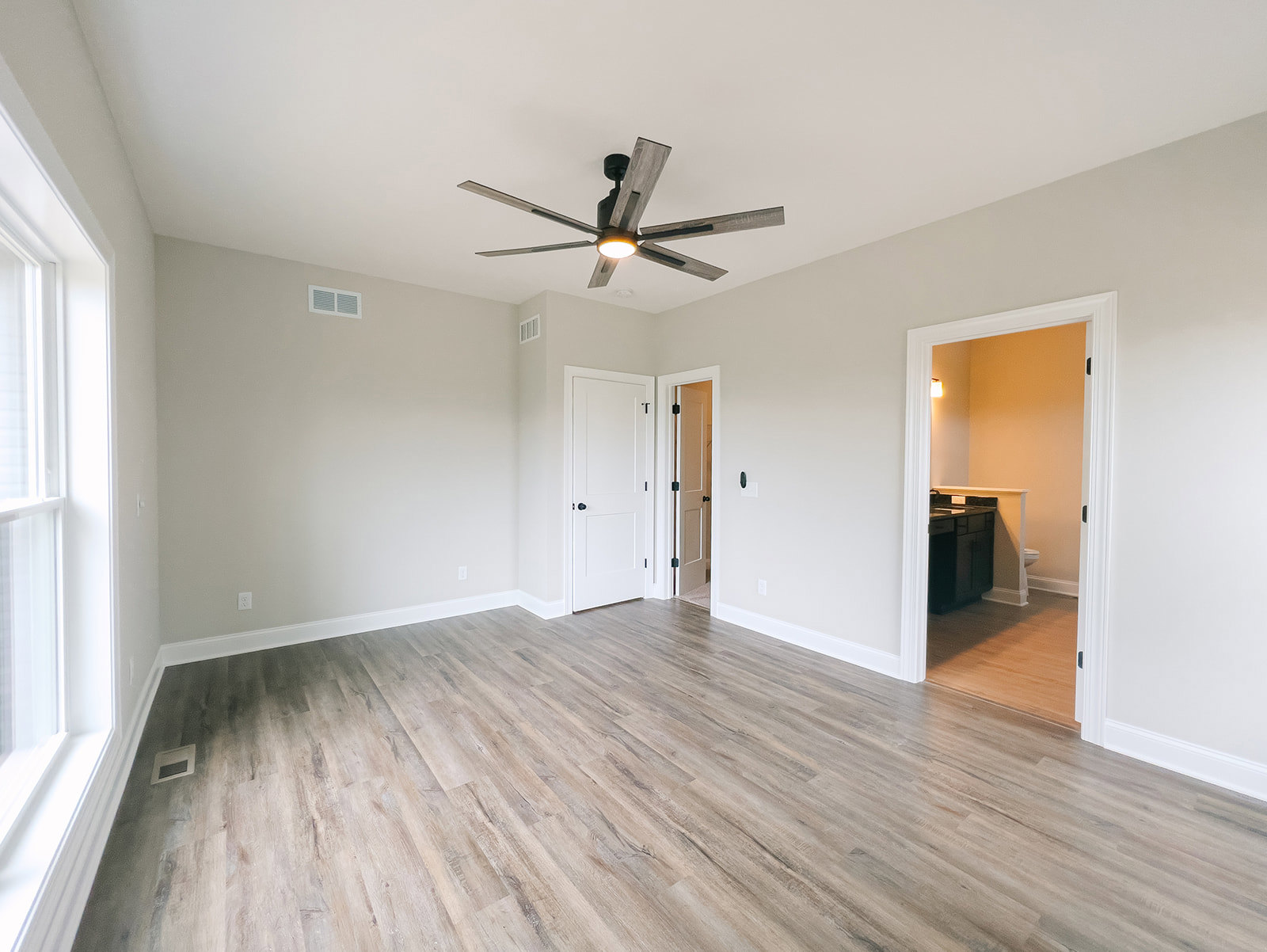 Ceiling fan with light fixture mounted on white plaster ceiling, wood laminate flooring, white door with black hardware partially open, white wall with electrical outlet and black