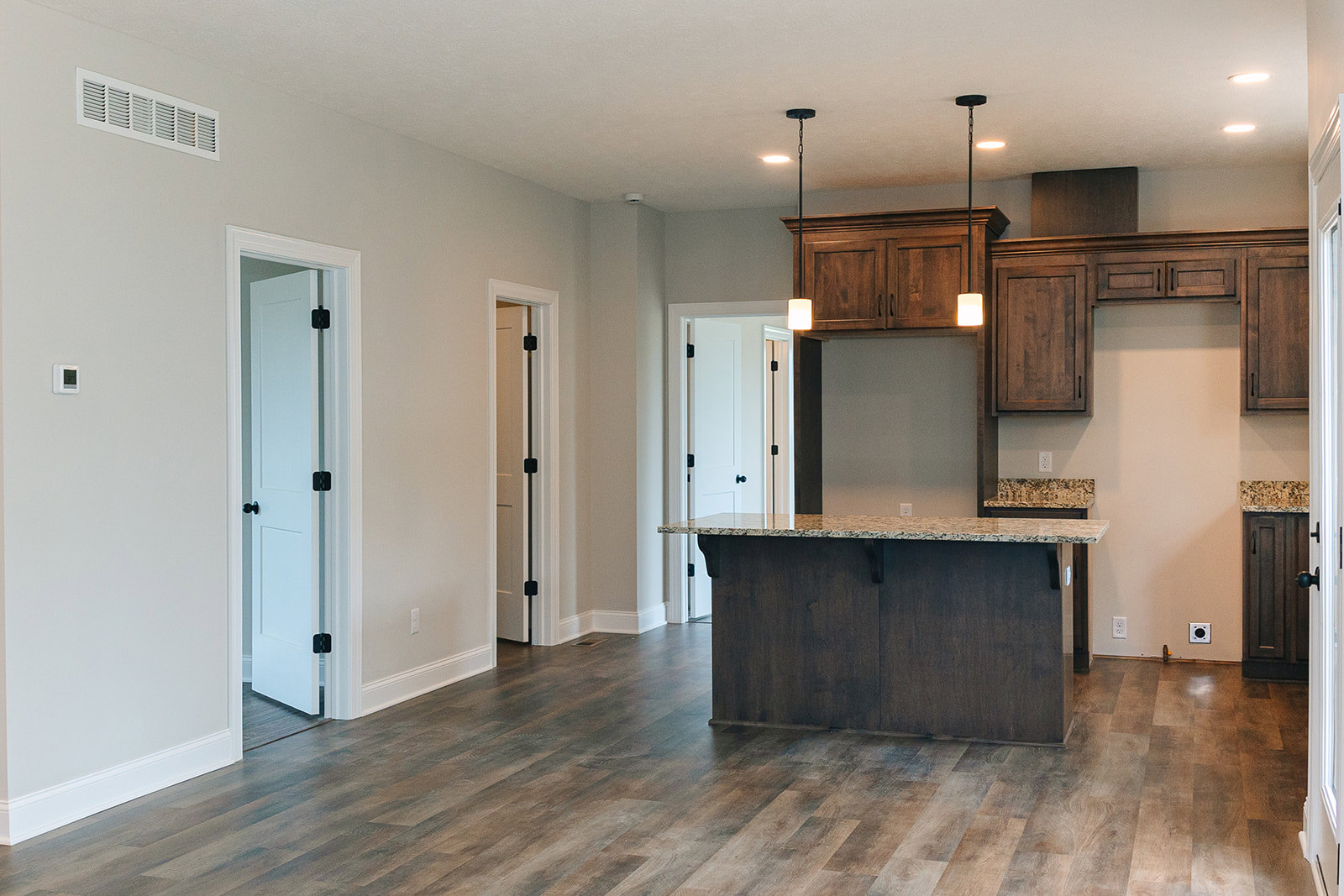 Kitchen with marbled countertop bar, wood-grained flooring, white cabinetry, black hardware, wall vent, and white door with black hinge and knob