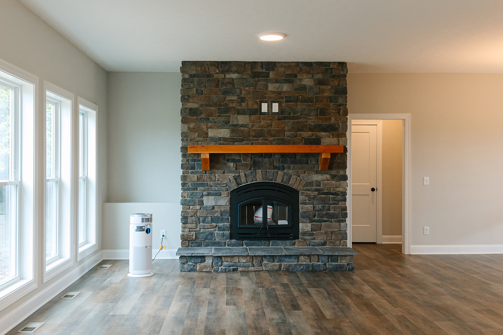 Stone fireplace with wood mantel, fire screen, and hearth set against a textured wall; adjacent white door with black hardware.