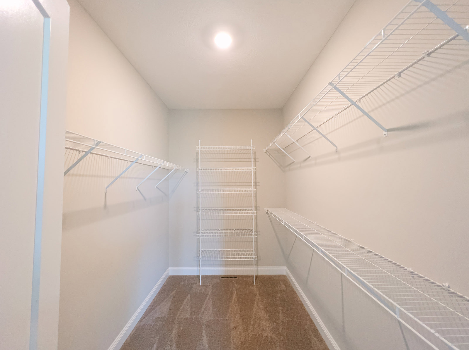 Carpeted closet with built-in white metal shelves, ceiling light fixture, and wall vent