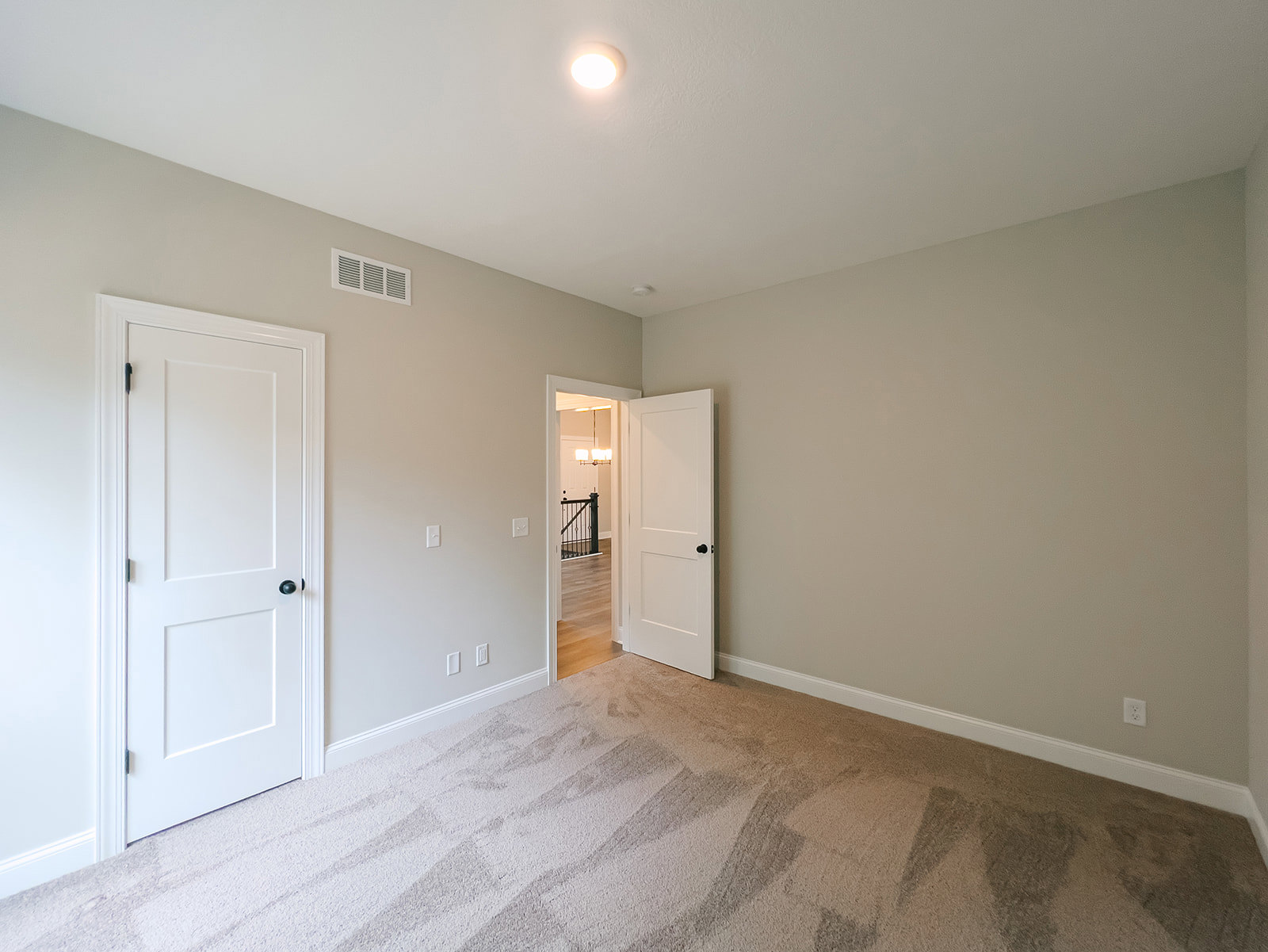 Carpeted room with two white doors featuring black knobs, ceiling light fixture, and close-up view of stair railing