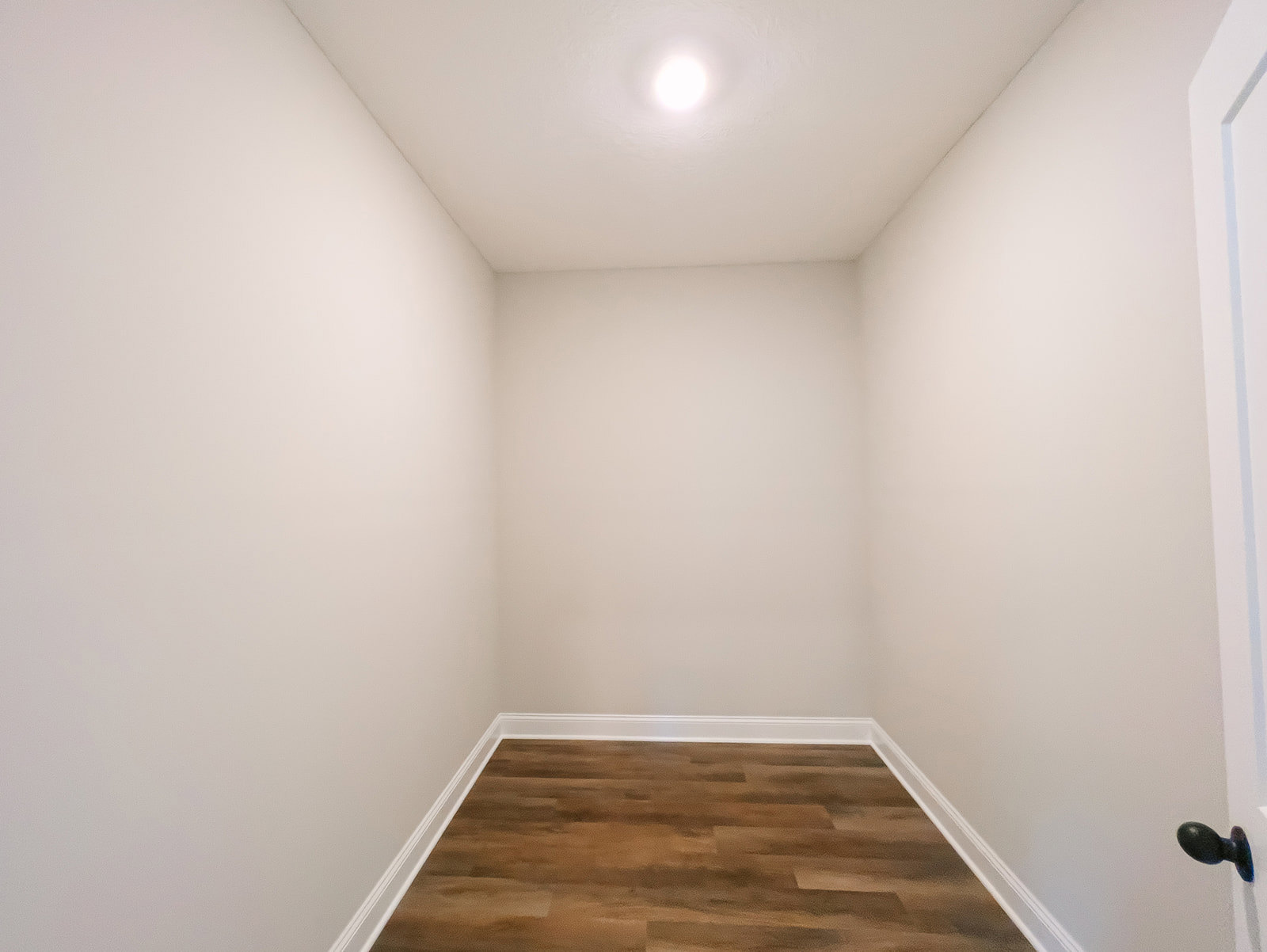 Wood flooring with white baseboards, white walls, ceiling-mounted light fixture, black door knob on white door