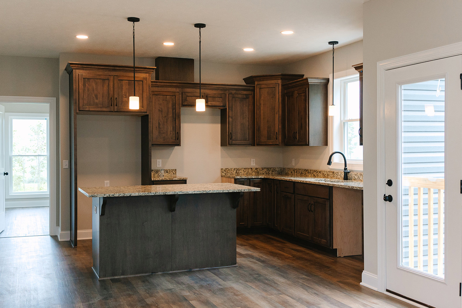 Marbled countertop with undermount sink, white cabinetry, tile backsplash, glass panel door, window, and black hardware accents