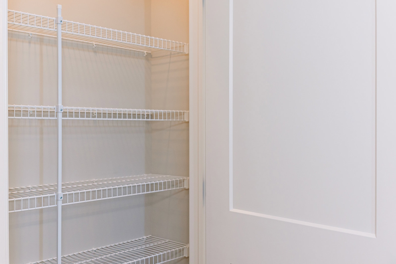 White closet interior with multiple white wire shelves and a white door with matching frame.