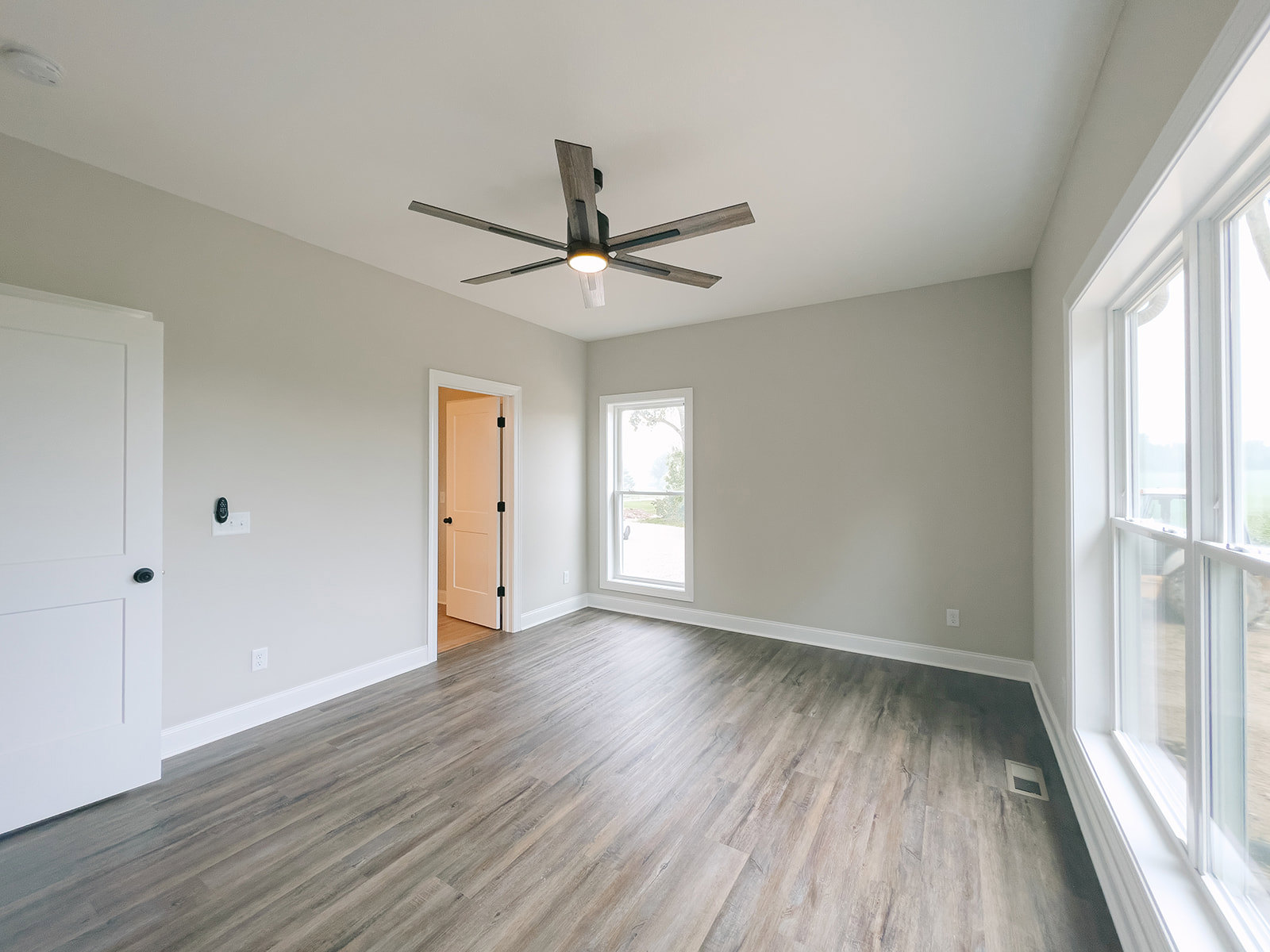 Ceiling fan with light fixture, hardwood floor, white door with black knobs, window overlooking green lawn, neutral walls
