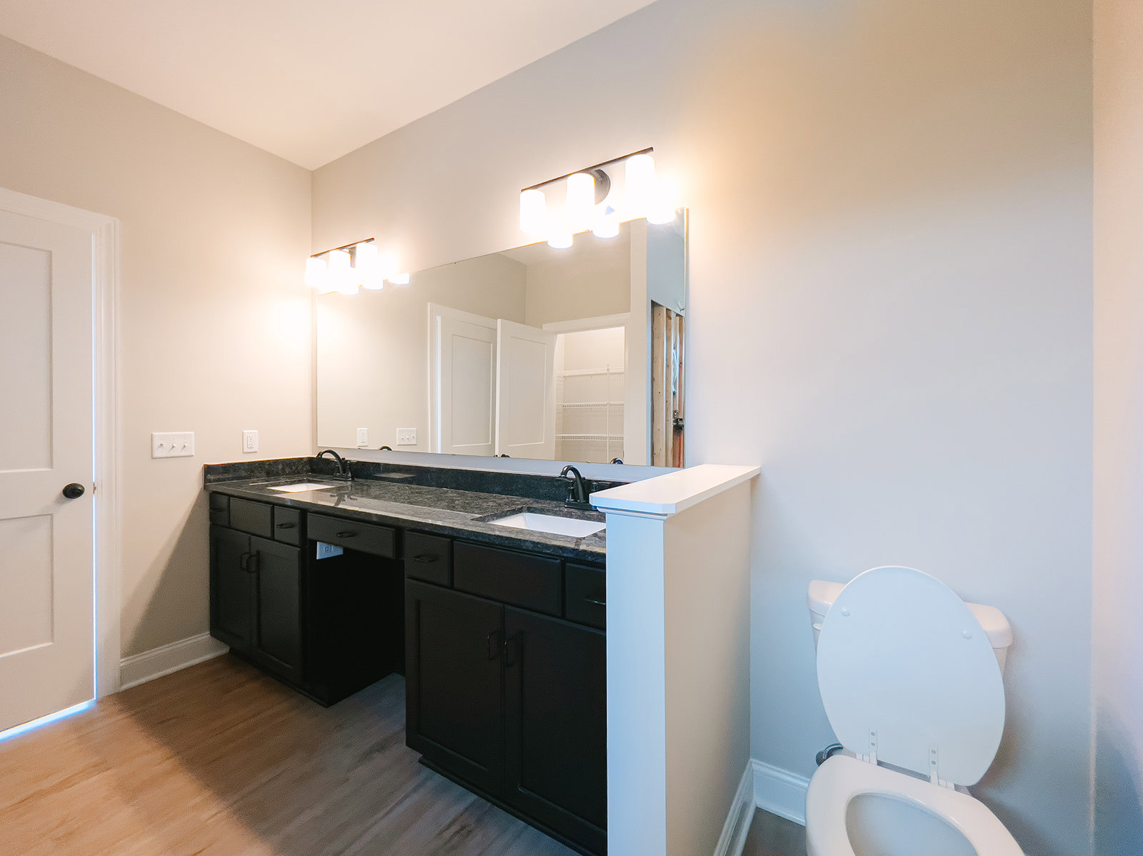 Bathroom with black countertop, black cabinet with handles, white toilet with lid up, white walls, tile flooring, and modern light fixture with white lights.