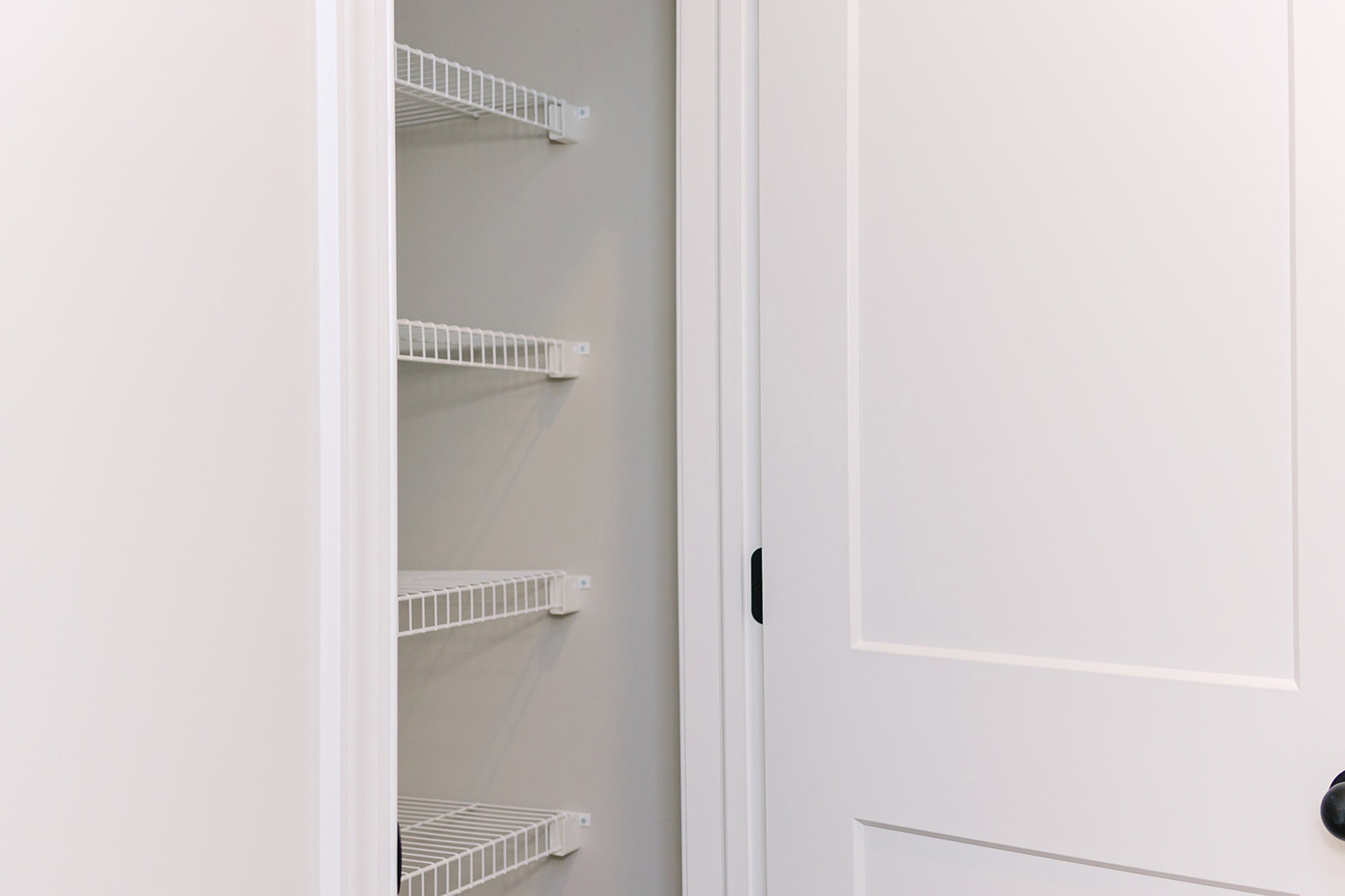 Walk-in closet with white wire shelving, white walls, and a white door featuring a black handle