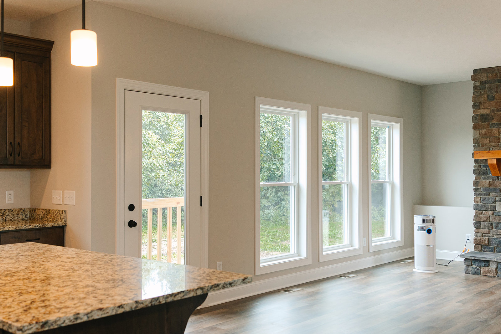 Marble countertop and island in a modern kitchen with white cabinetry, wood flooring, wall-mounted light fixture, and large window overlooking trees