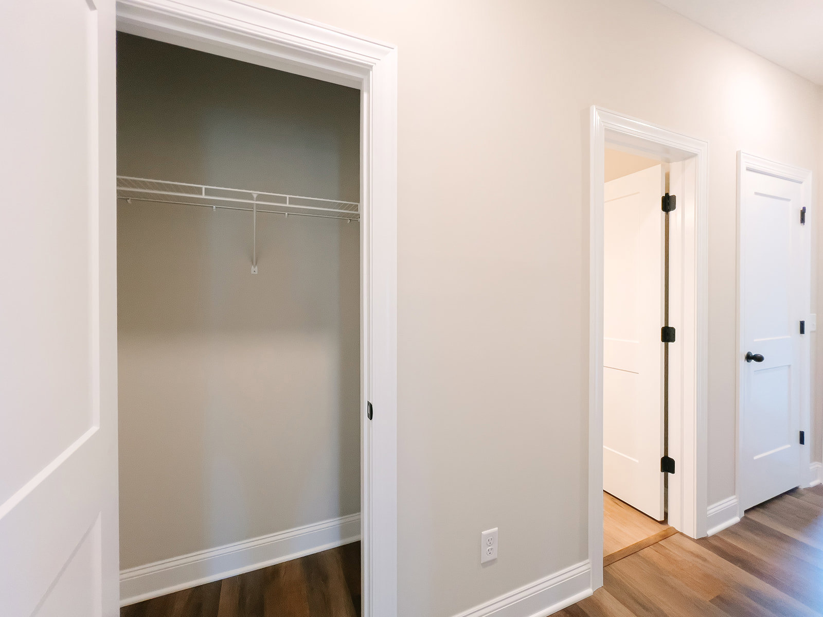 Walk-in closet with open white door, black handle, built-in white shelving, white walls, and black trim