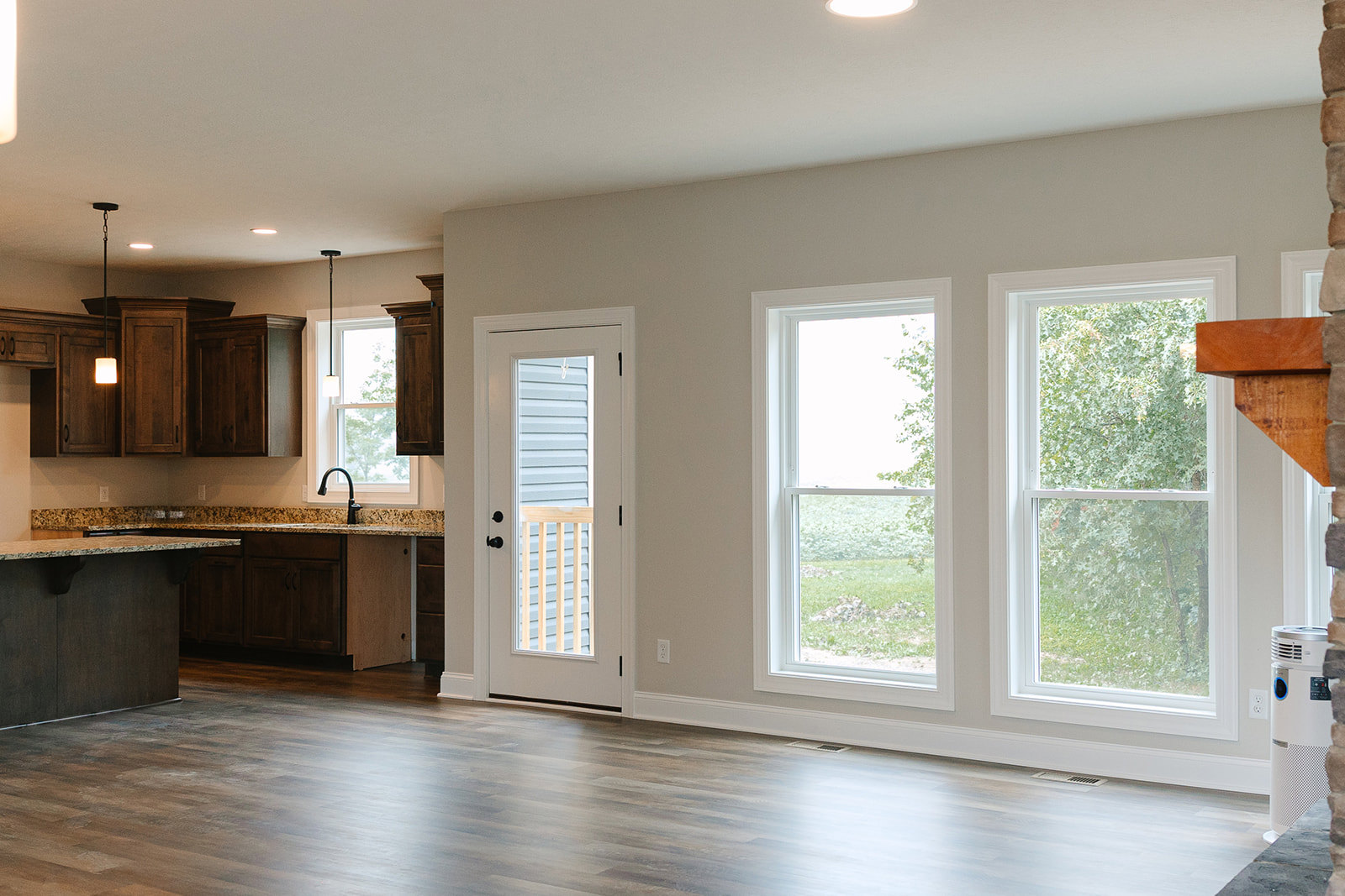 Open kitchen and living room featuring white walls, wood flooring, white cabinetry, stone countertop, window overlooking a field, white door with glass panel and railing, pole