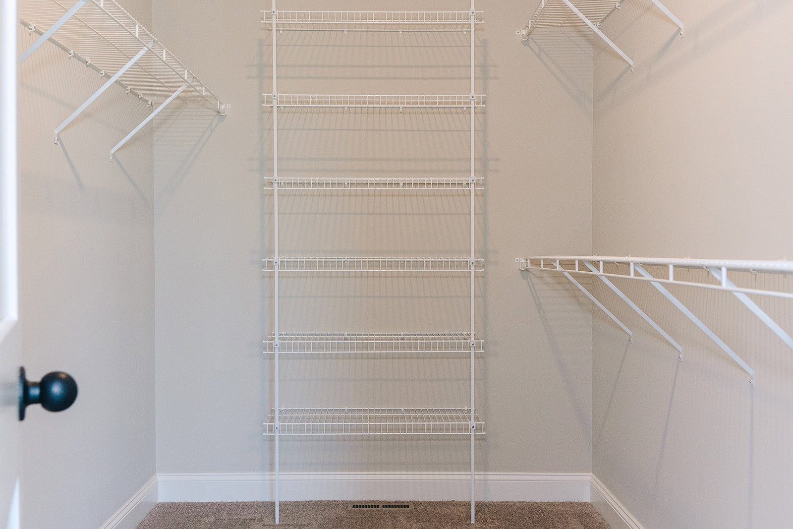 White wire shelf with hooks mounted on plaster wall near door with silver knob in residential interior.