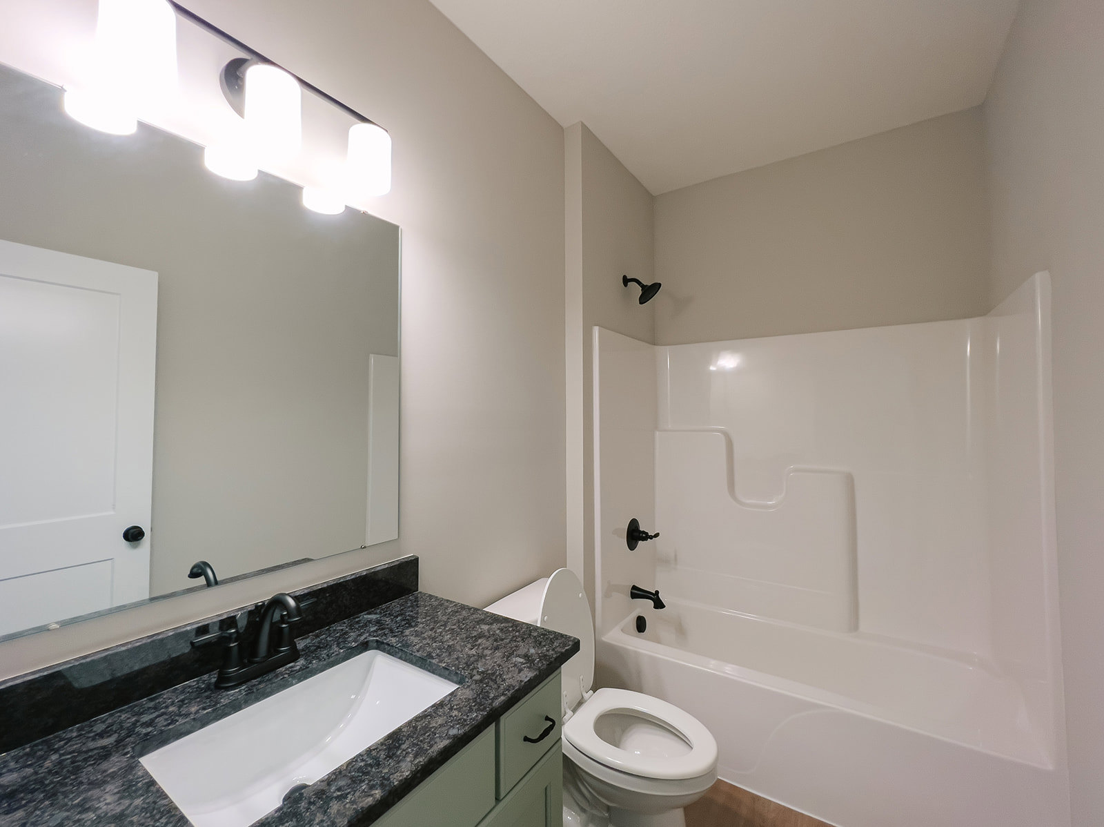 White tile bathroom with freestanding bathtub, black faucet sink, wall-mounted row of lights, and toilet