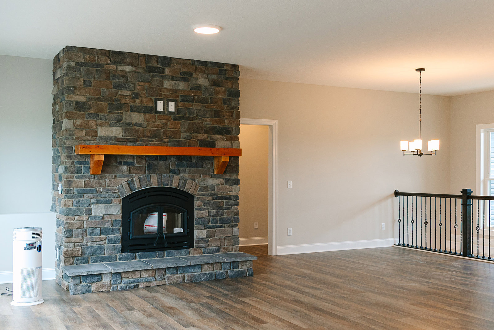 Modern brick fireplace with wood mantel, fire screen, and white bag of material on hearth, surrounded by light flooring and metal railing in a contemporary living room.