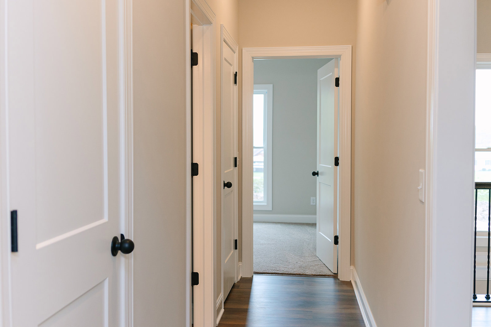 Hallway with white paneled doors, wood flooring, and black door handles