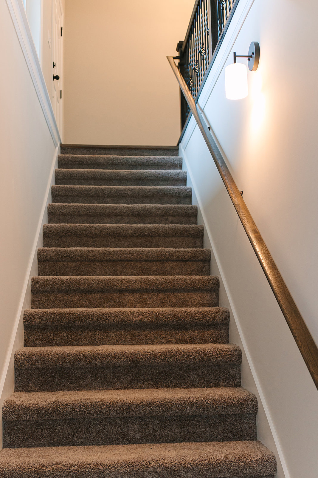 Carpeted staircase with wooden handrail and white balusters, adjacent to a neutral painted wall