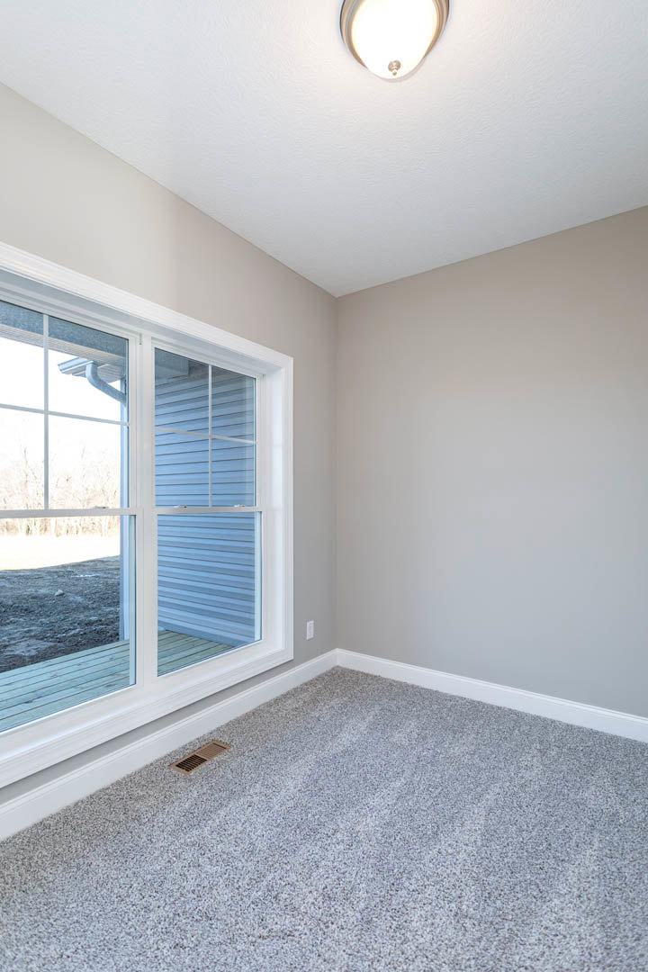 Bedroom with grey carpet, white walls, ceiling light fixture, window featuring white blinds and outdoor view, floor vent in corner