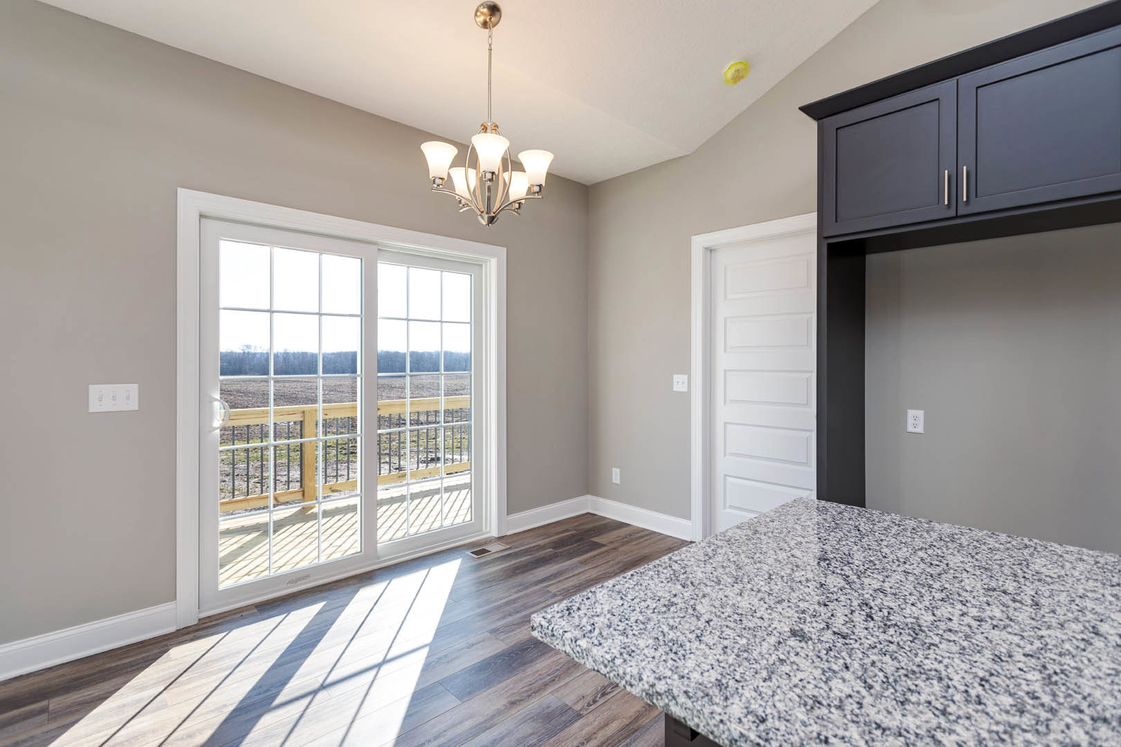 Marble countertop with white cabinetry, sliding glass door opening to deck and field view, wood flooring, modern chandelier, and lamp.