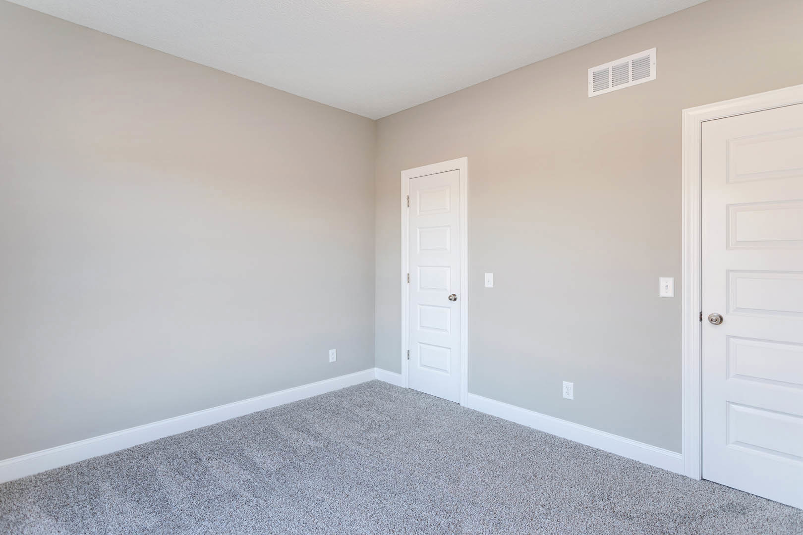 White paneled door with silver knob, beige carpet flooring, white walls, ceiling vent, and crown molding in a residential room