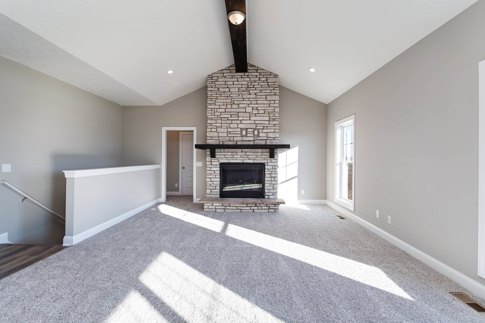 Carpeted living room featuring a white fireplace with a black mantel, white door with black handle, wall-mounted light fixture, and large window