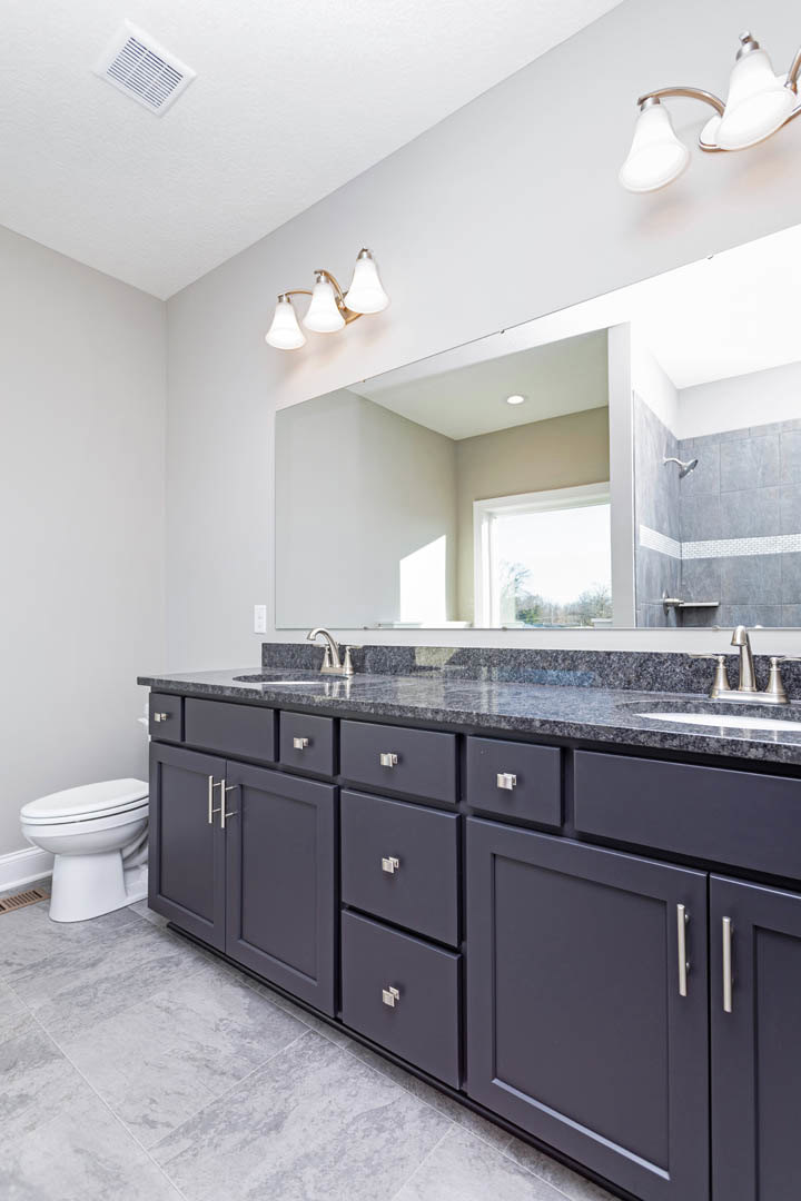 Bathroom with expansive mirror above dark wood cabinets, white countertop with undermount sink, three-light wall fixture, closed toilet, tile flooring, and chrome hardware