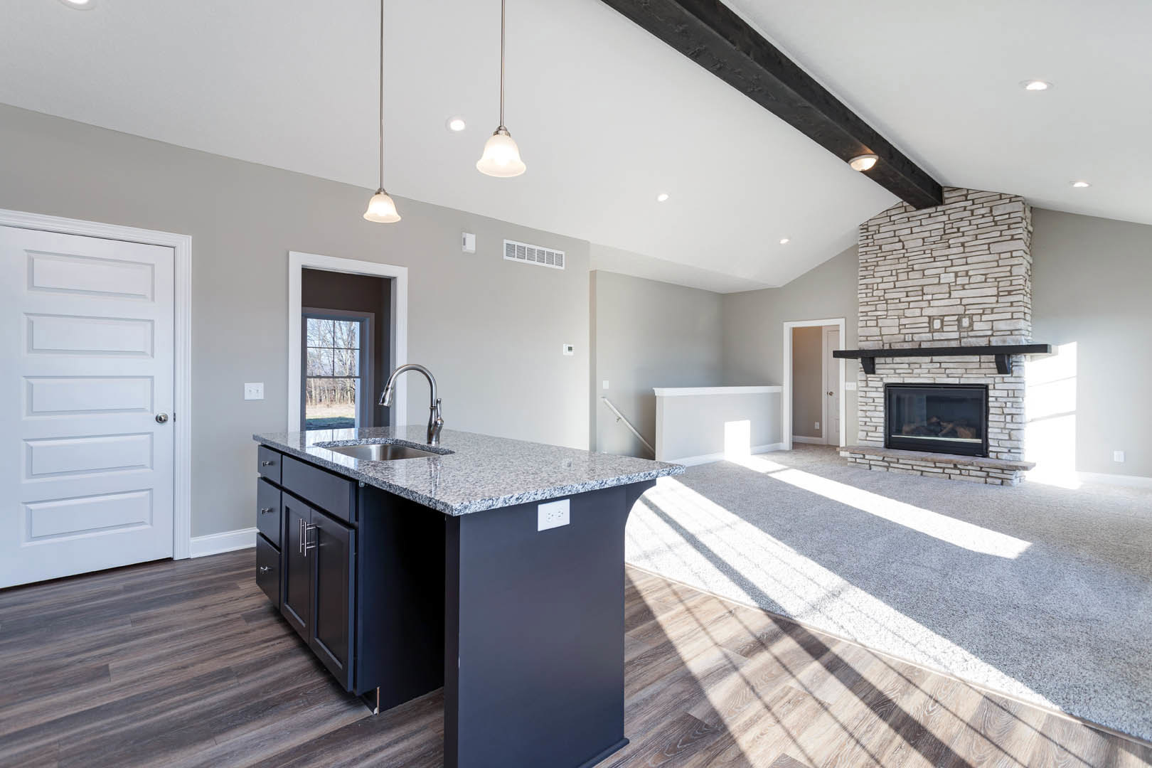 Open-concept kitchen and living room featuring a brick fireplace, wood flooring, white cabinetry, kitchen island with sink, and white door with black trim