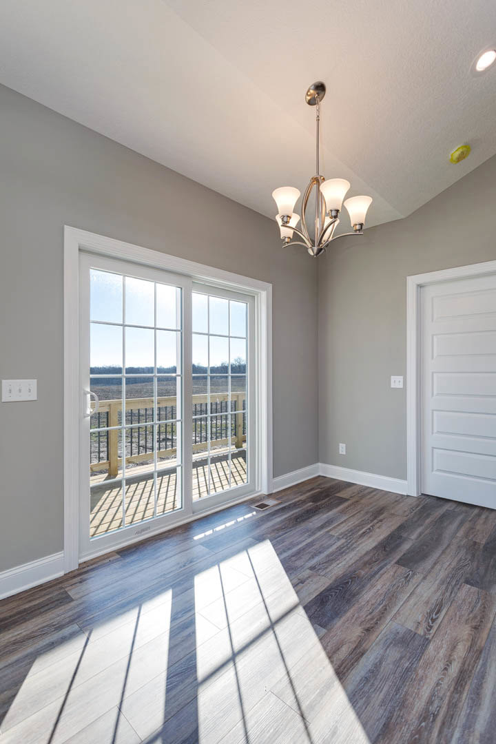 Open room with light wood flooring, white walls, white door, sliding glass door, large window, and modern chandelier.