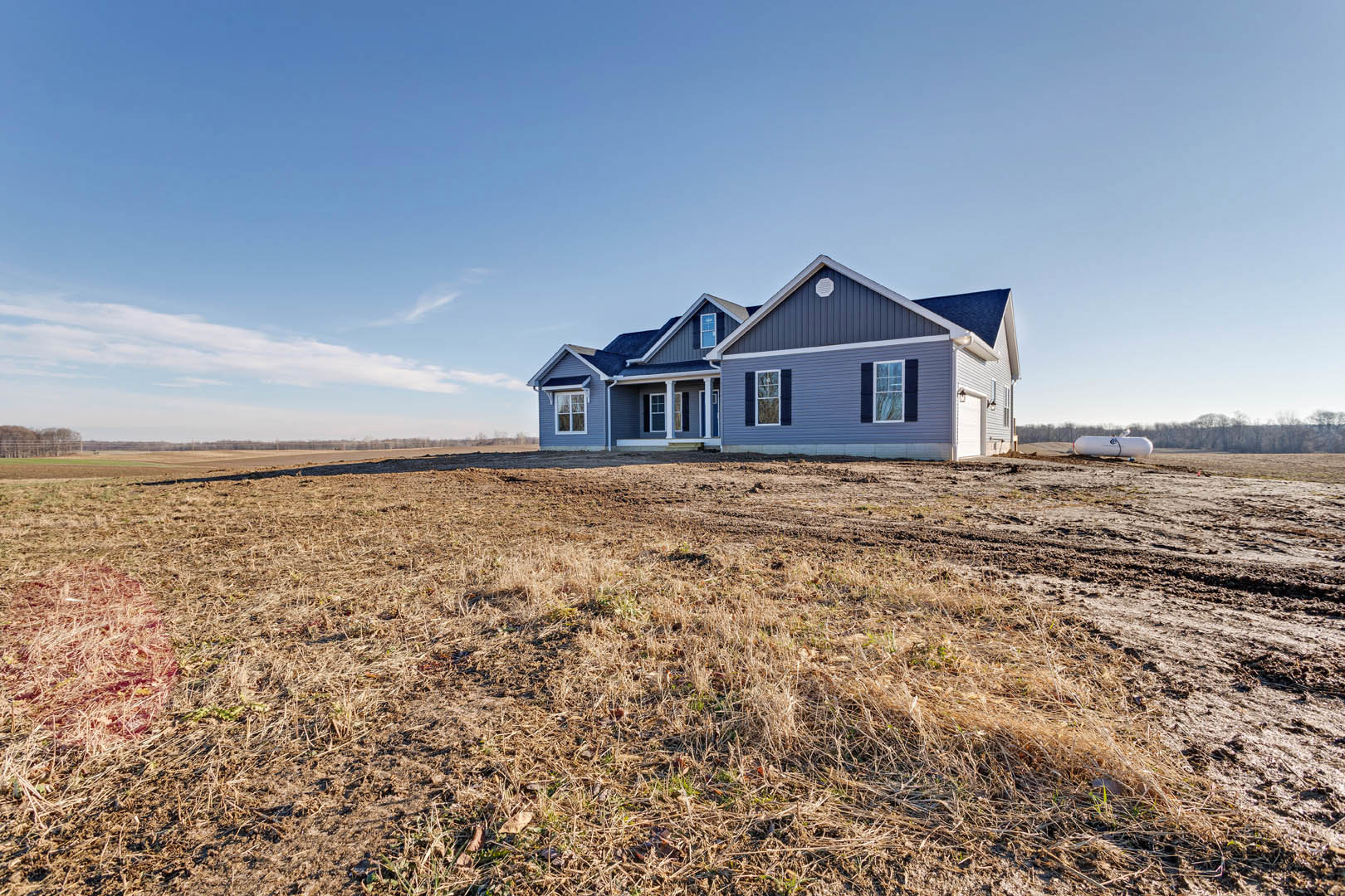 Two-story house with white siding and covered porch, set on a spacious grassy lawn under a clear blue sky