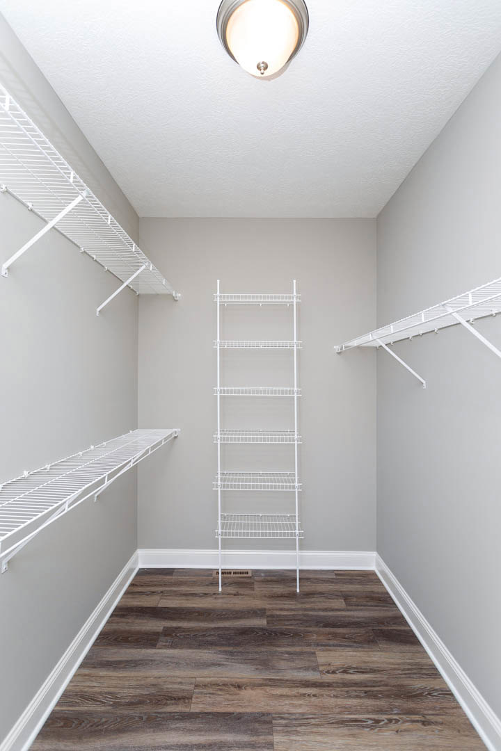 White metal shelving units mounted on plaster walls, wood flooring with white railing, ceiling light fixture, and white shelves supported by metal rods.