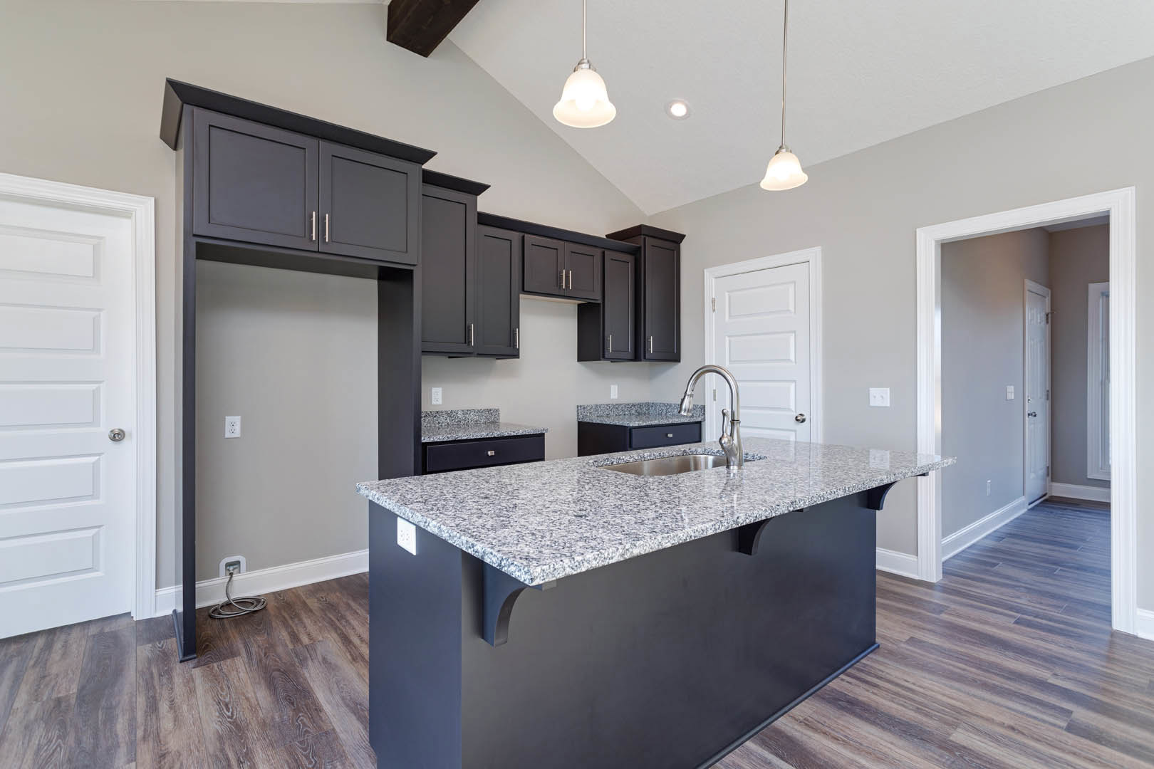 Granite kitchen island with built-in sink, white cabinetry, tiled floor, and modern lighting fixtures