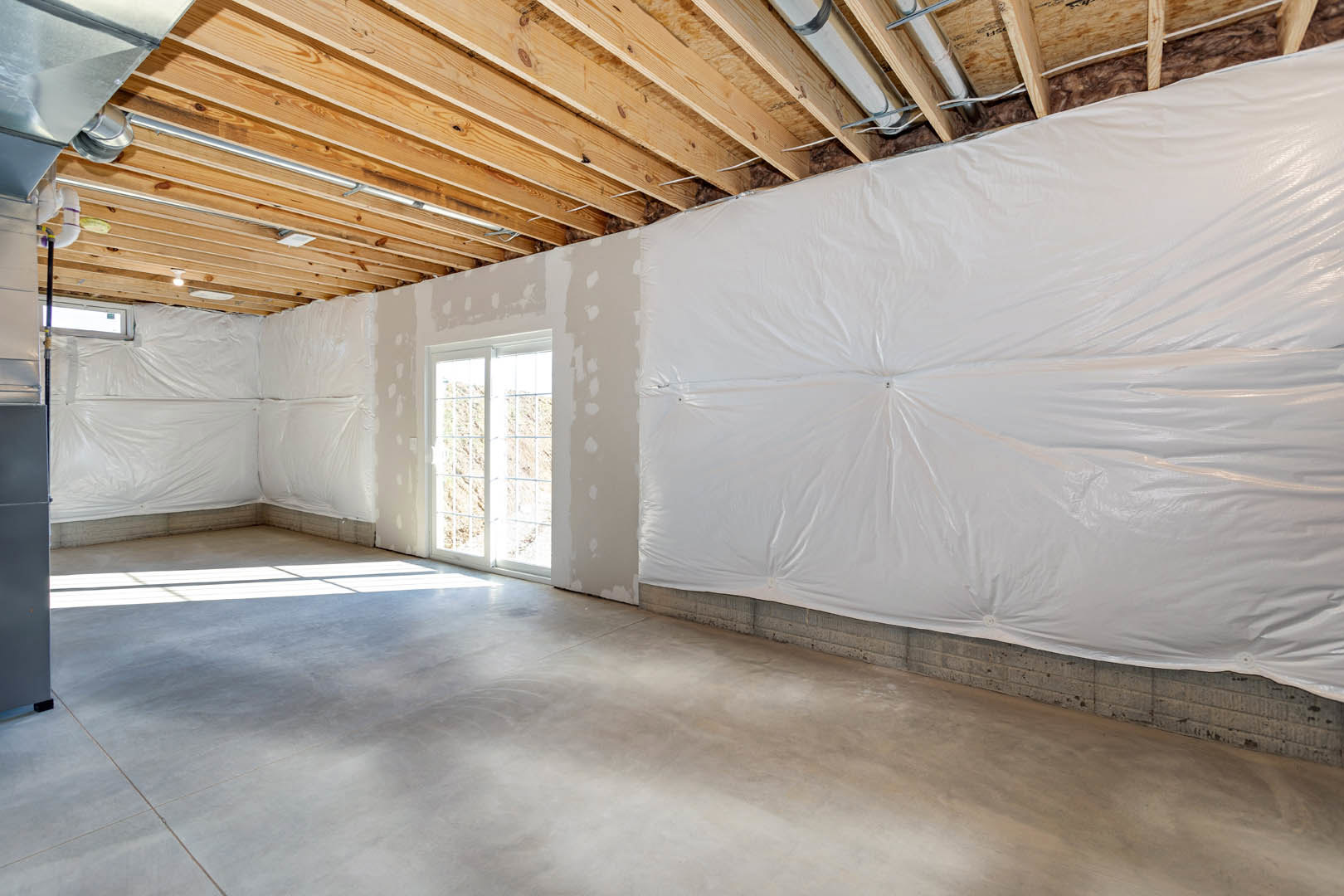 Room under construction with white plastic wall coverings, white sheet covering the floor, wooden ceiling partially wrapped in white material, and a window framing mountain views.