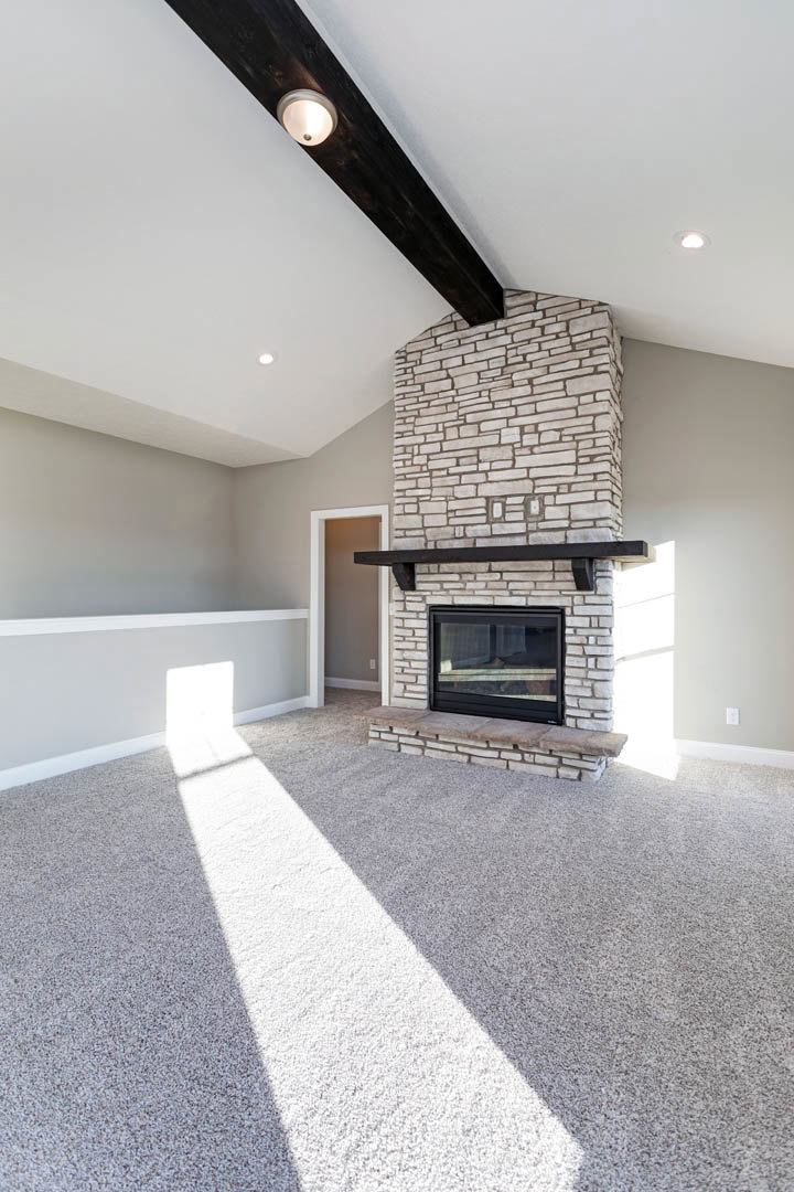 Carpeted living room featuring a white fireplace with a black mantel, sunlight streaming through a large window, and recessed ceiling lights