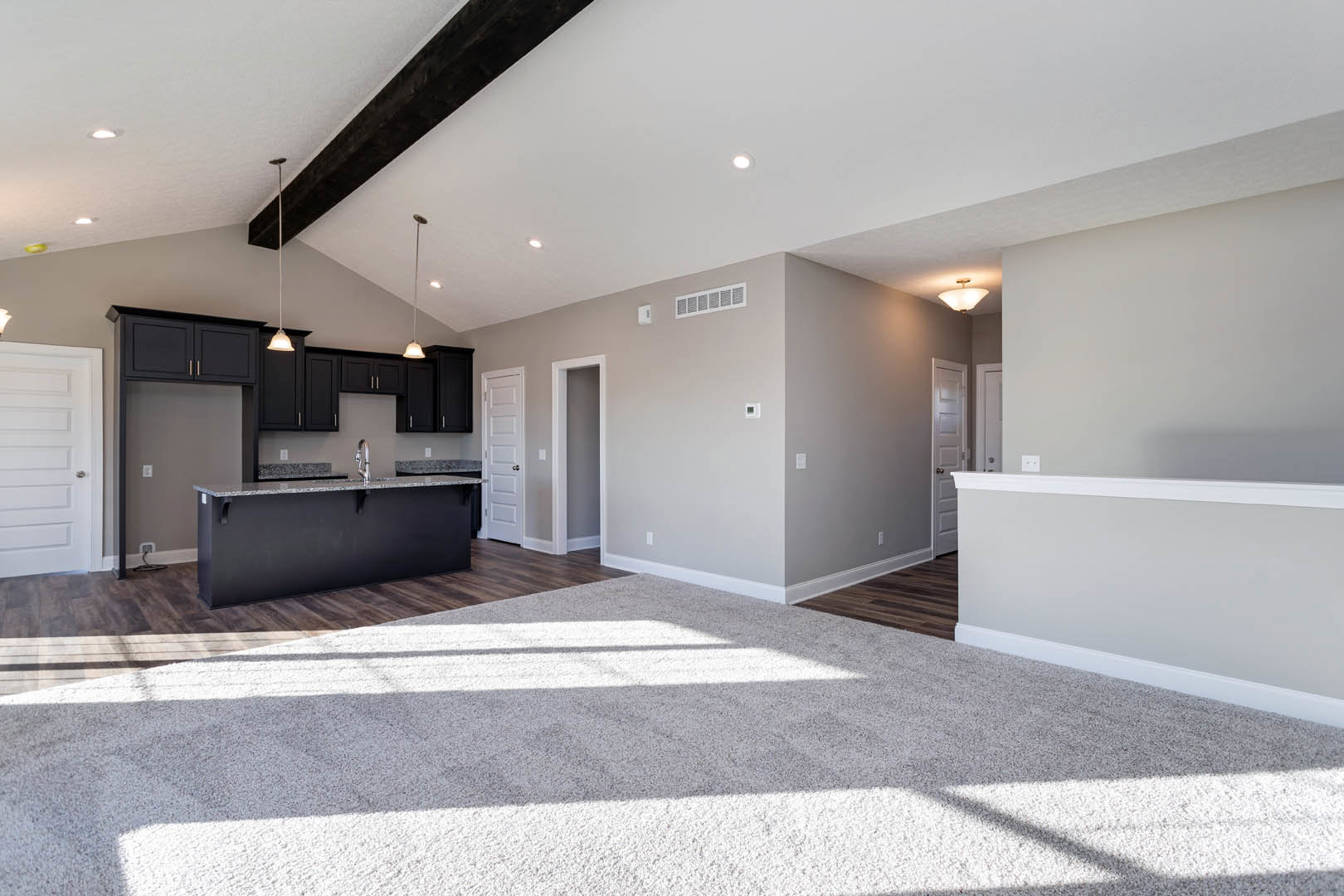 Open kitchen and bar area with black countertop and sink, white carpeted floor, grey walls, recessed ceiling lights, white door with silver knob, and white doorway.