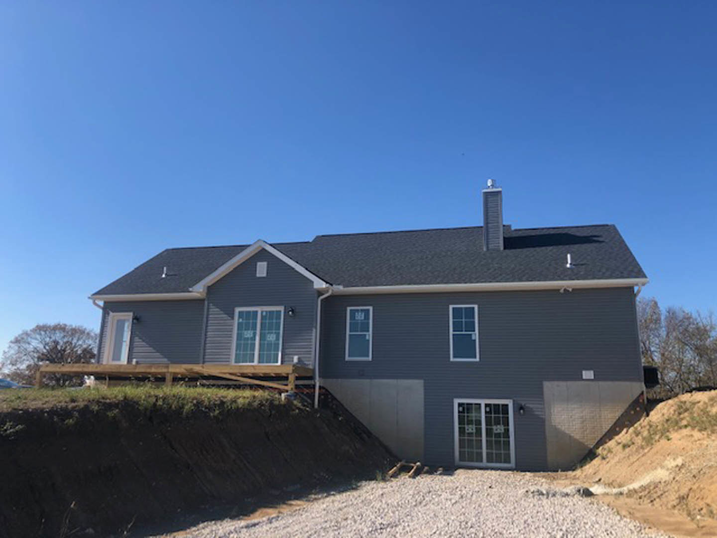 Partially built house with exposed framing, white window frames, ramp leading to entrance, situated on a hill under clear blue sky