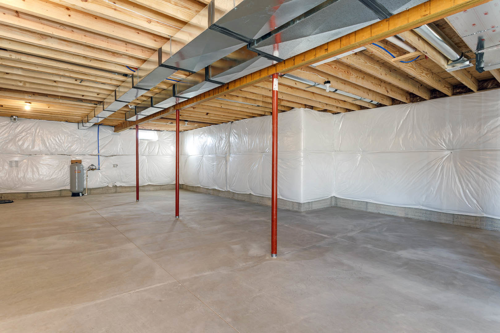 Room with white walls, wooden ceiling beams, concrete floor, red metal poles, and white plastic coverings along the walls.