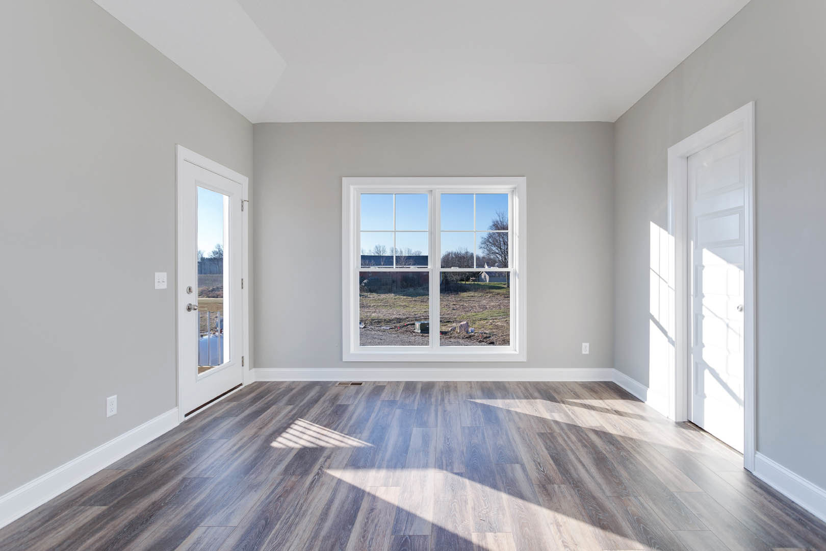 Room with wood flooring, white walls, large window overlooking a field, and white doors with silver handles