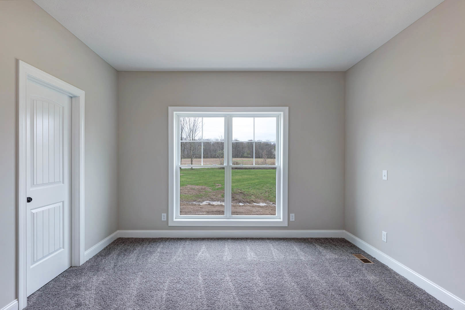 Bedroom with light gray carpet, white walls, large window overlooking grassy field, white door with black handle
