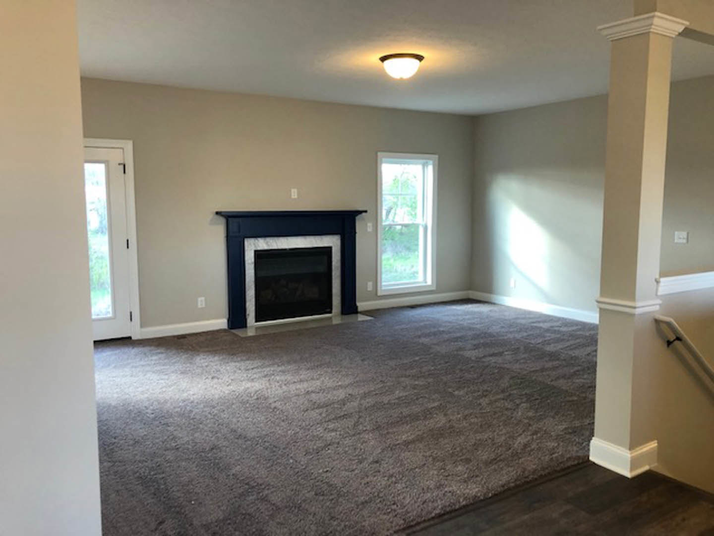 Living room with light-colored carpet, white-framed window, black-framed glass fireplace, and white door set in plaster walls