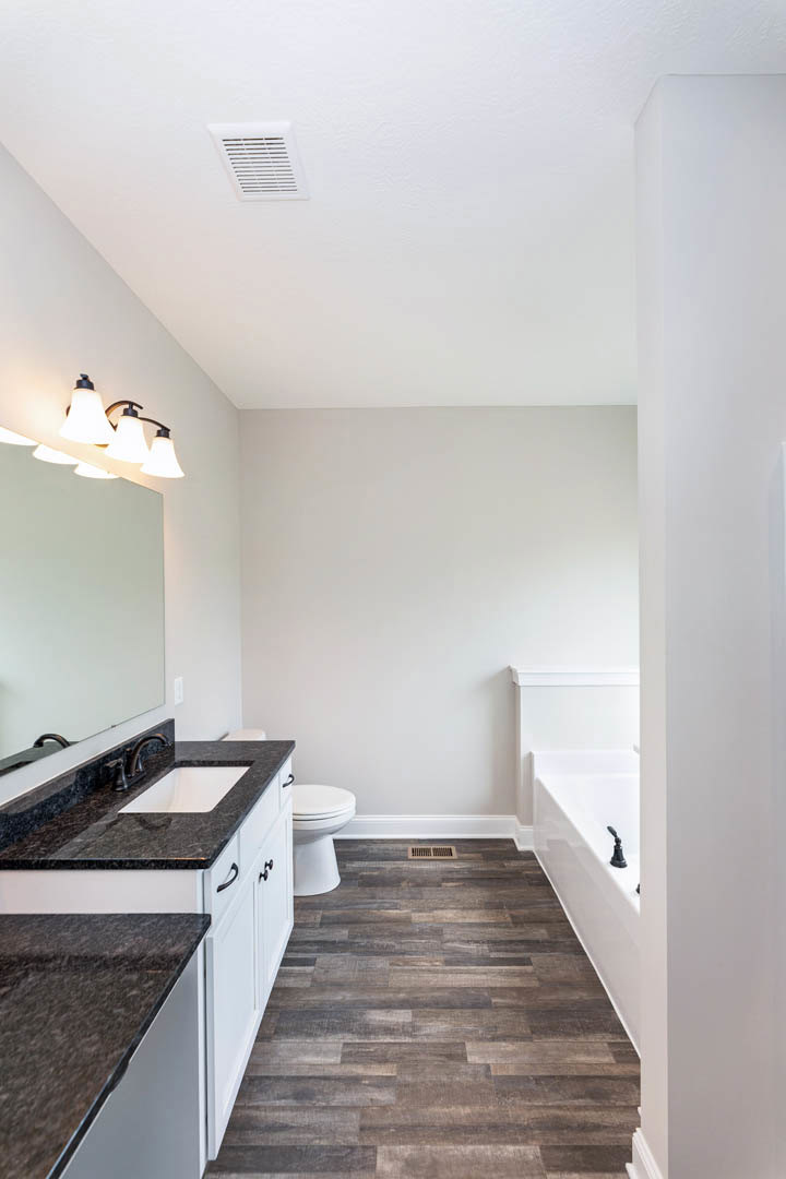 Bathroom with freestanding bathtub, wood flooring, white countertop with sink, modern light fixture, and white toilet against tiled wall