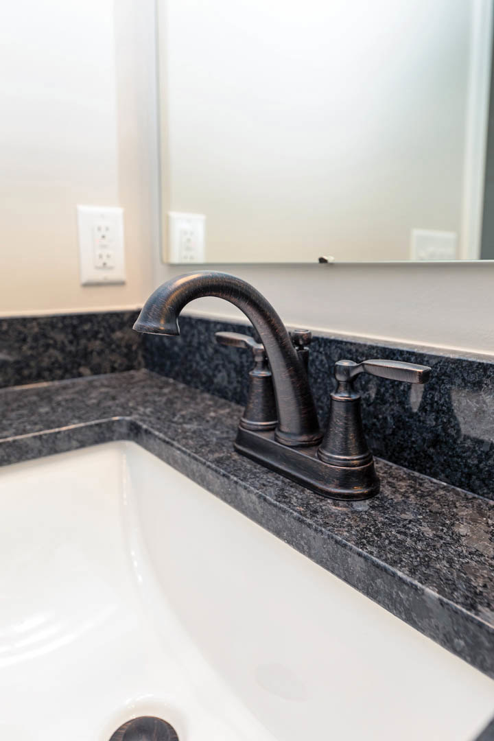 Matte black faucet mounted on white sink, white countertop, minimal white wall with framed pictures and black-button outlet in background