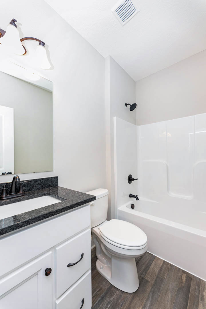 Modern bathroom featuring a white porcelain sink with chrome faucet, matching toilet with closed lid, light gray tile walls, white cabinetry, and a vent with blue accents.