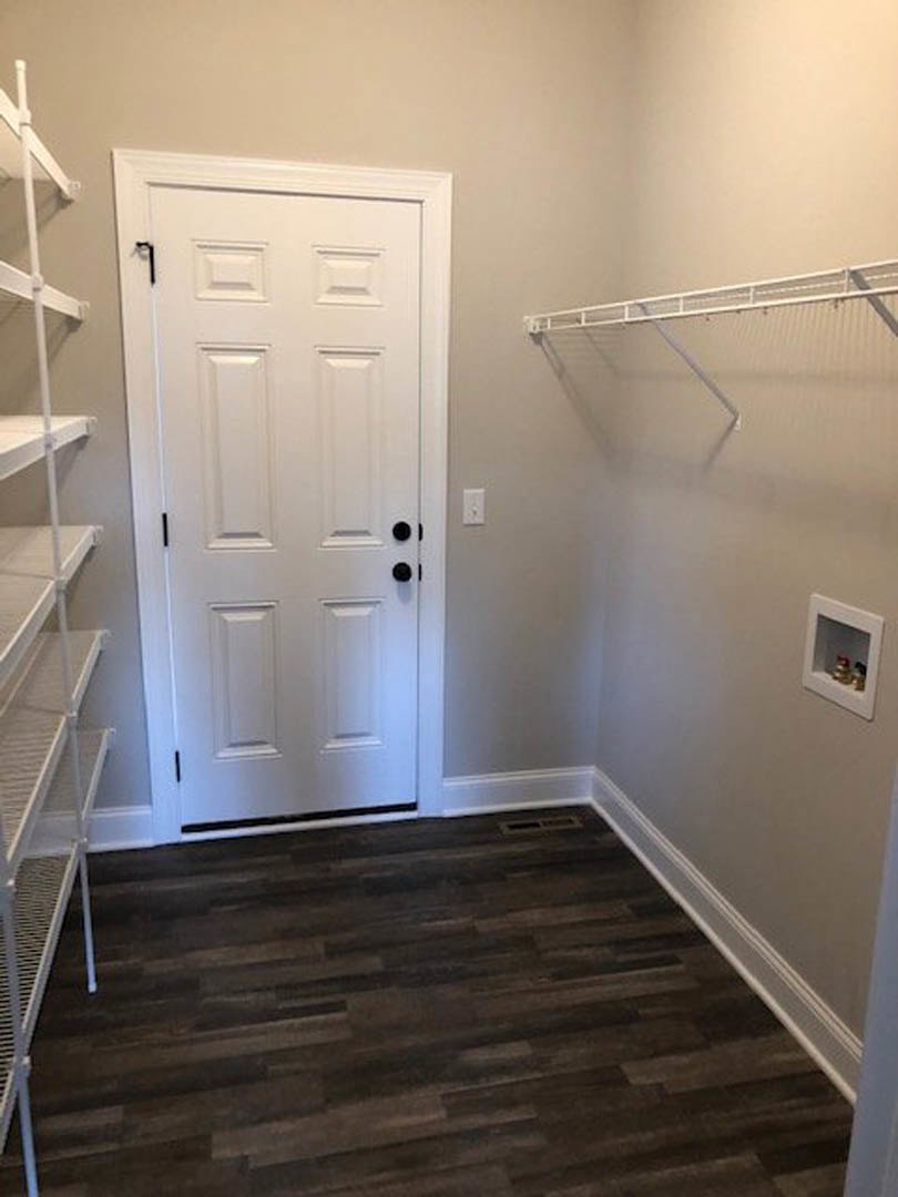 White door with black knobs set in a white wall, dark wood flooring, white staircase with metal railing, black border trim.