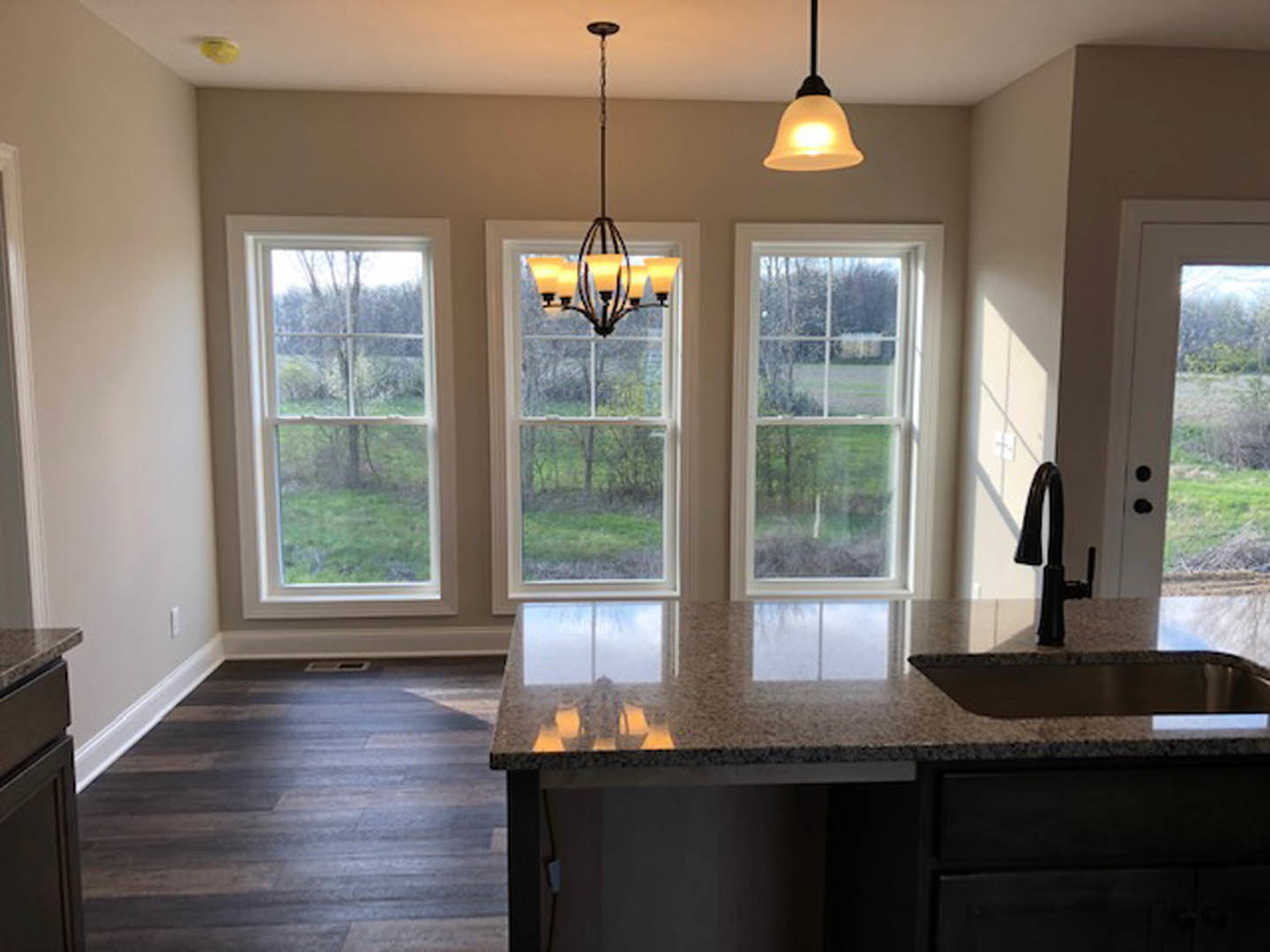 Marble kitchen countertop with dark wood flooring, white trim, large windows, white cabinetry, and modern chandelier