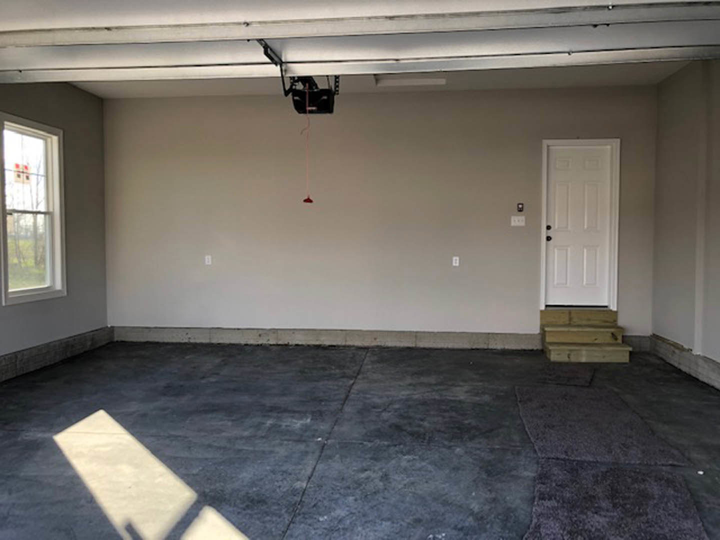Garage with two white doors, black hardware, adjacent window, concrete floor, and visible plaster walls.