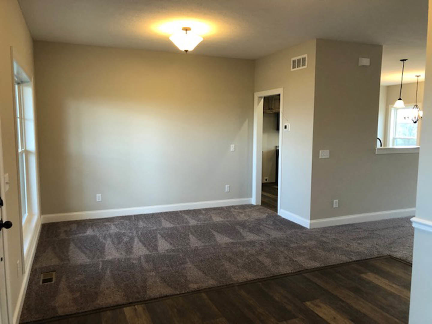 Neutral-toned carpeted room with white walls, recessed ceiling light, window with wall vent, and paneled door