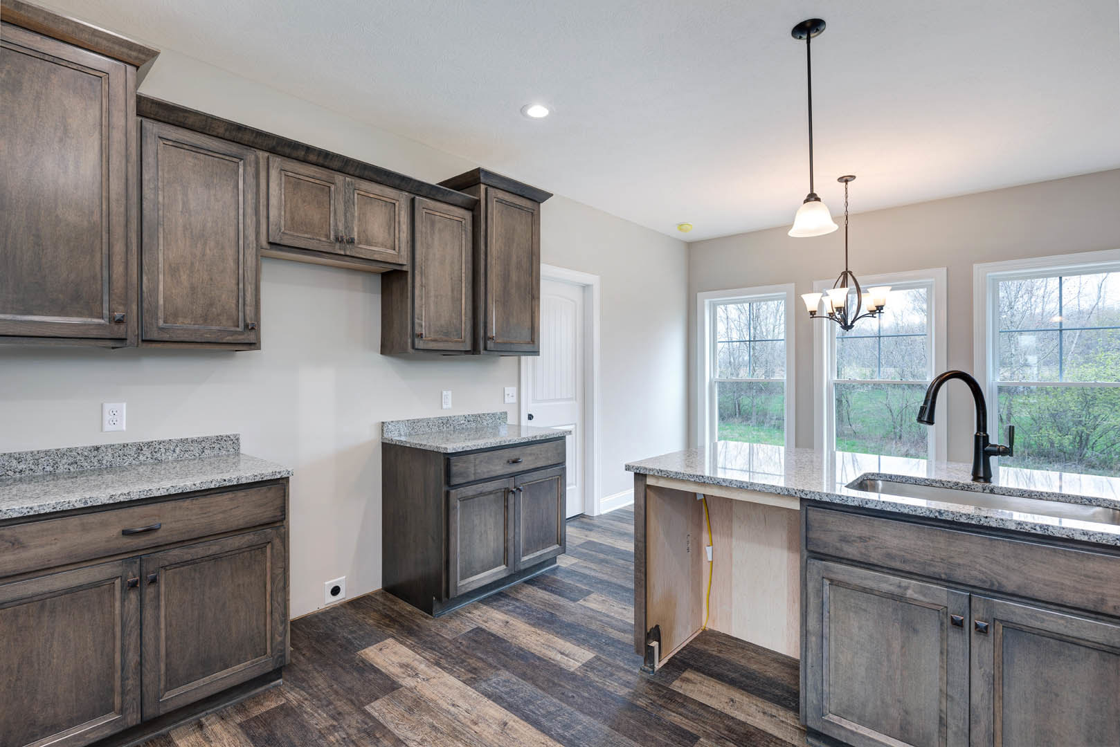 Granite countertops with white tile backsplash, dark wood cabinetry, stainless steel sink, and black faucet in a modern kitchen