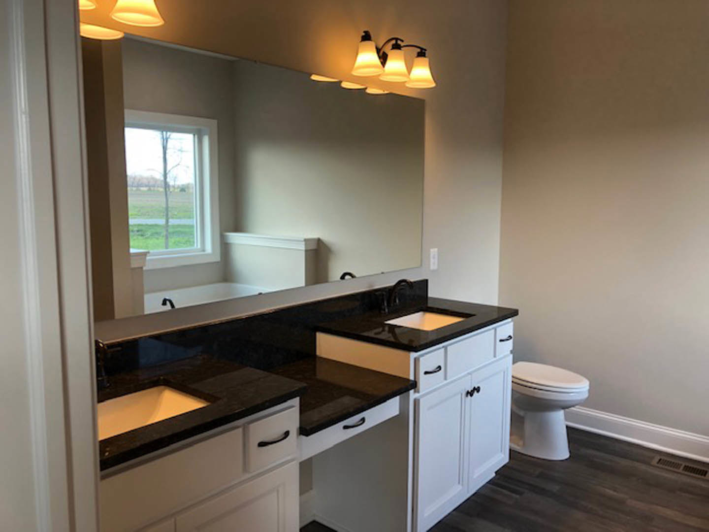 Double vanity with rectangular mirrors, white sinks set in light stone countertop, dark wood cabinetry, white toilet, neutral tile flooring